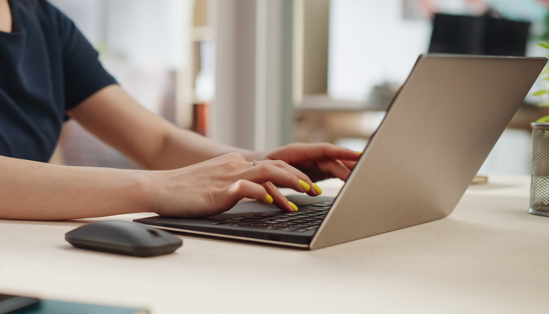 Photo of woman typing on a laptop. Her nail are painted yellow.