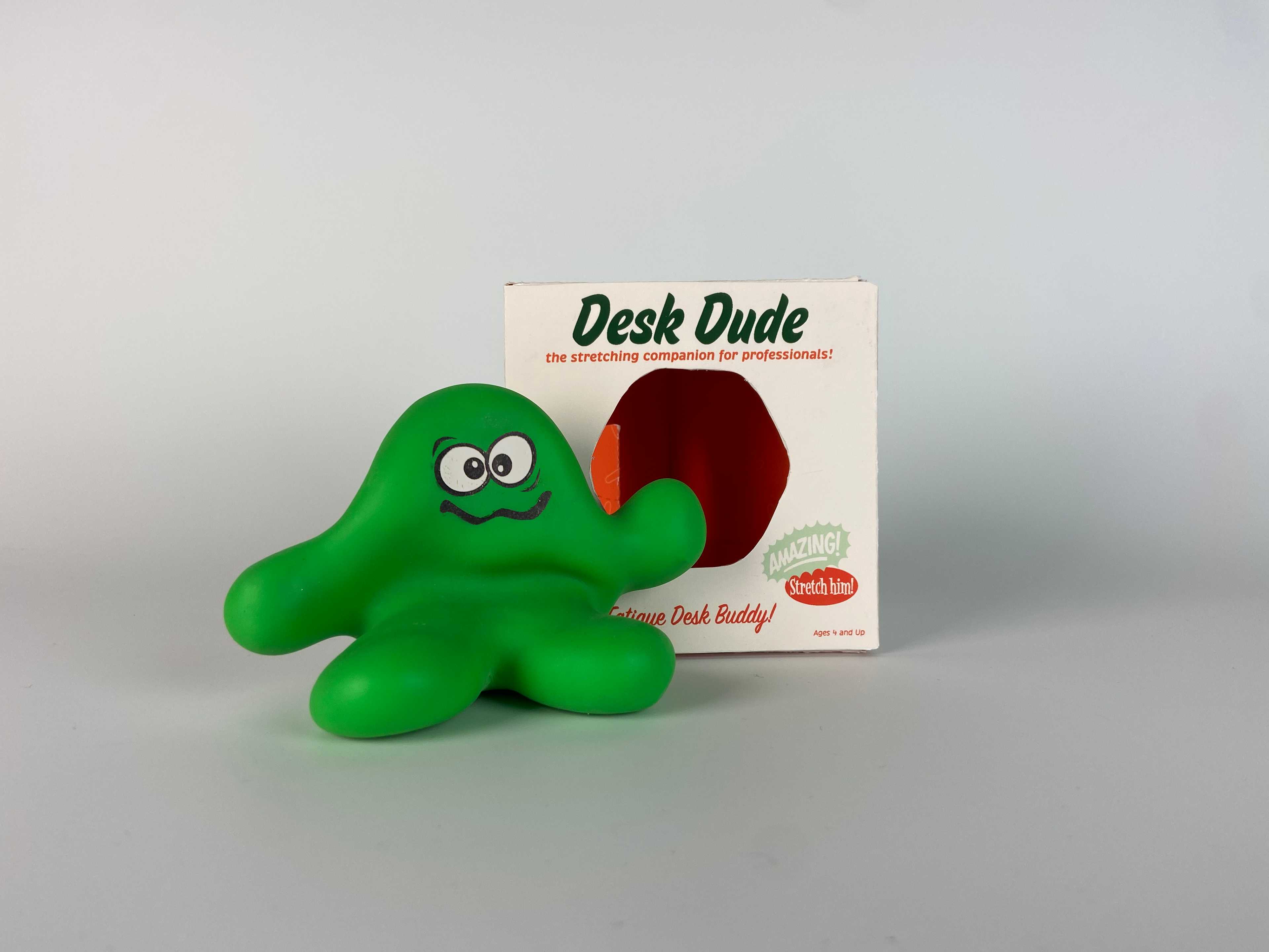 a green blob creature with a face sits in front of its packaging