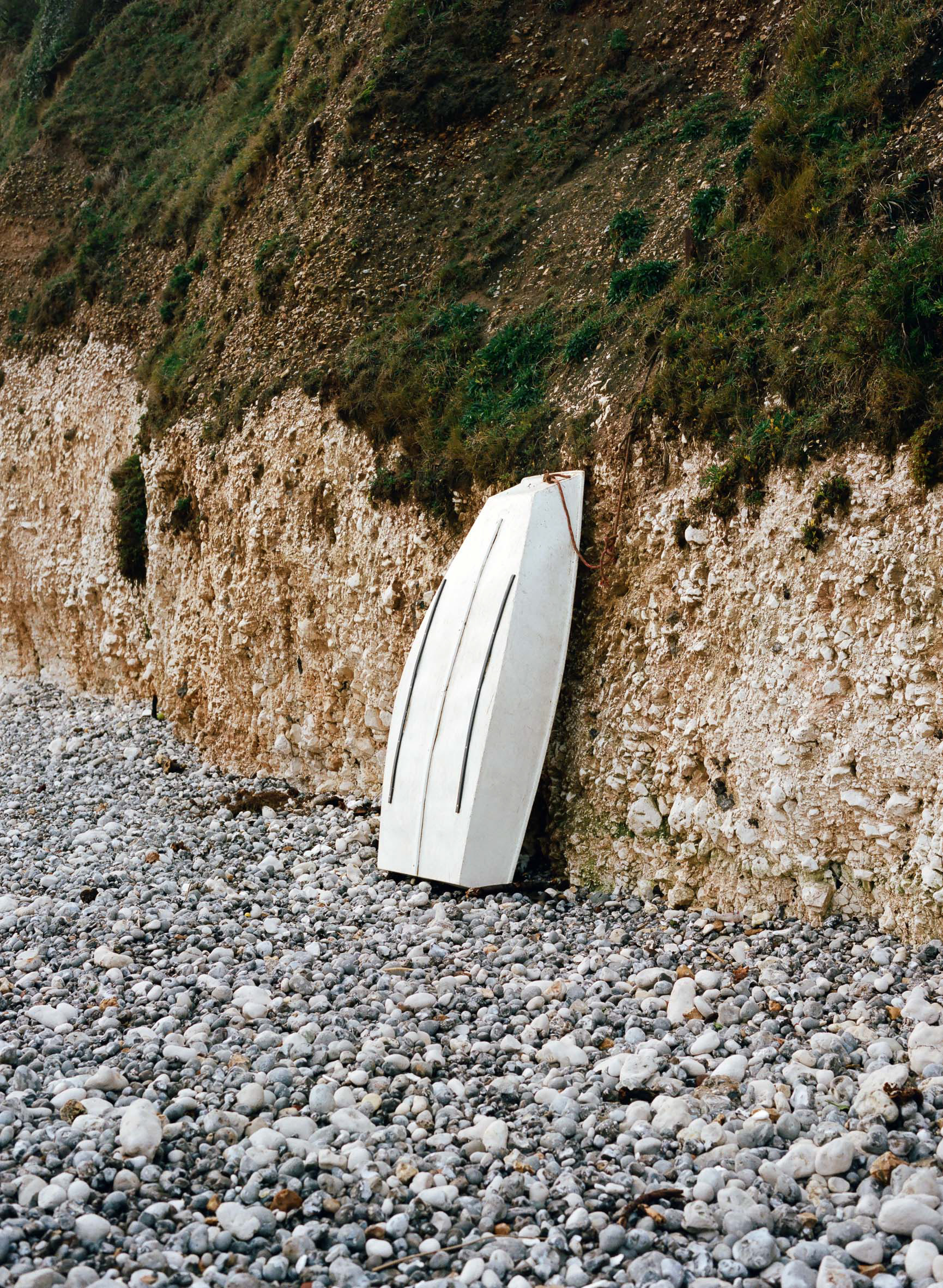 A small boat rests upright against the cliffs at Freshwater, Isle of Wight. A medium format photograph taken by Bristol based photographer Jake Hitchcock.