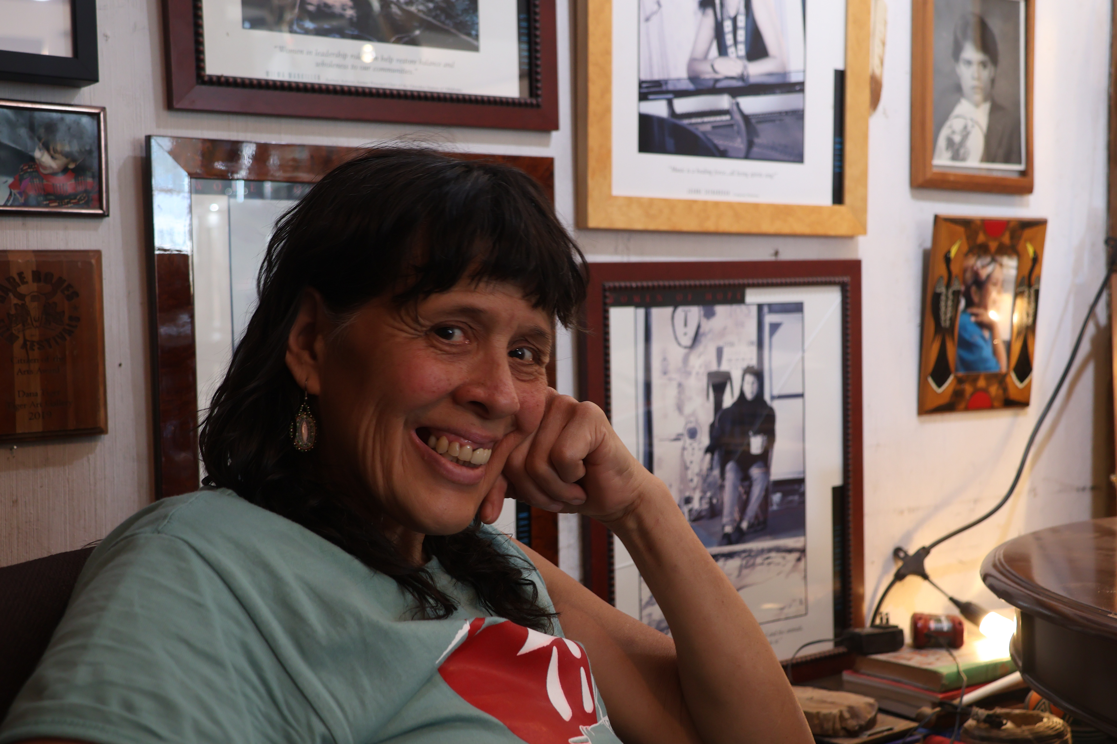 Dana Tiger smiles at the camera in front of a wall of art in Muskogee, OK. Tabitha Hidalgo