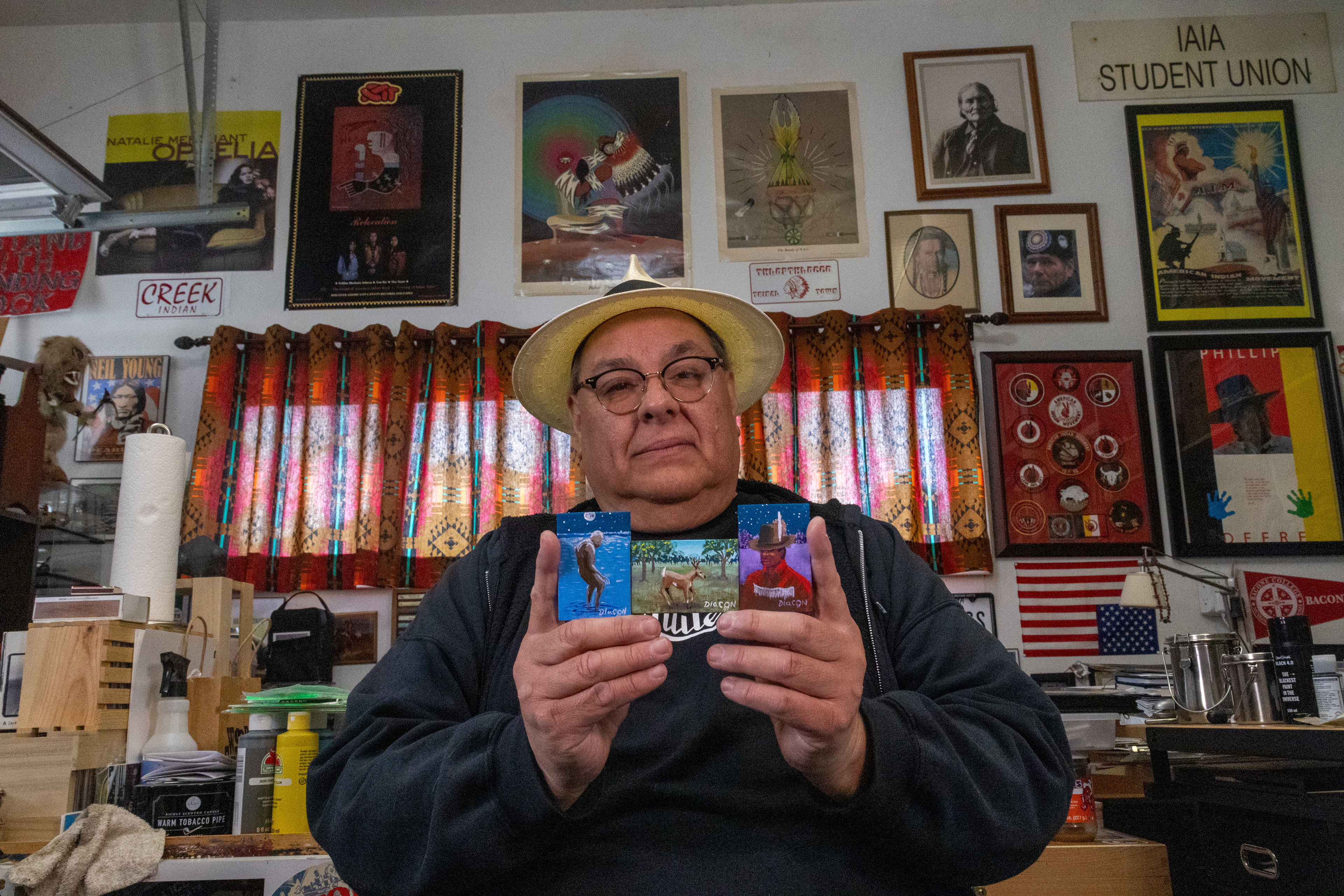Diacon holding three small paintings of bigfoot, a deer, and a medicine man. He only paints on small canvases so that his community and other people can afford to buy his artwork as most of his artwork is large scale and expensive. Elena Andra Stoica