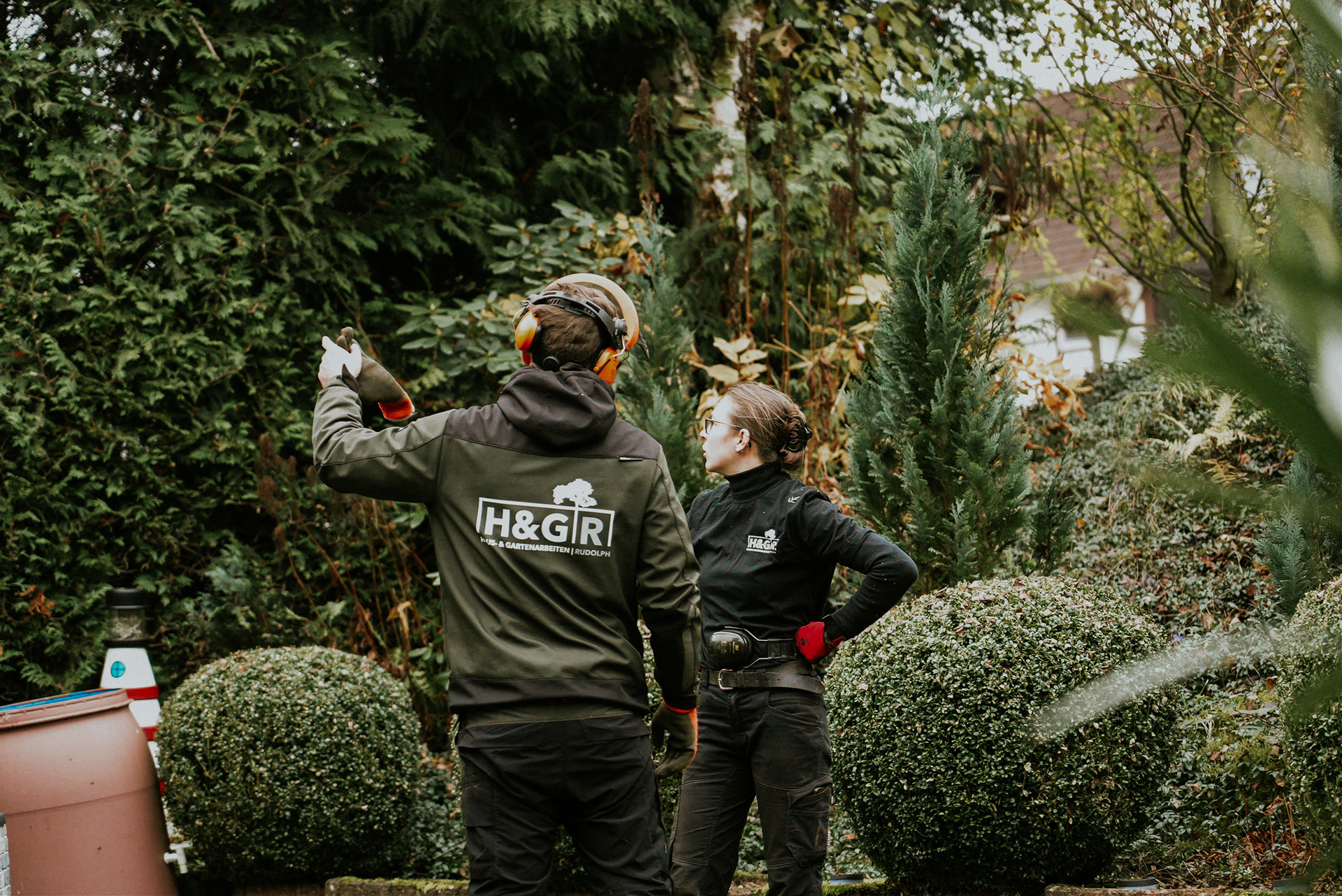 Zwei Gärtner von HG Rudolph bei einer Lagebesprechung in einem gepflegten Garten mit grüner Bepflanzung.