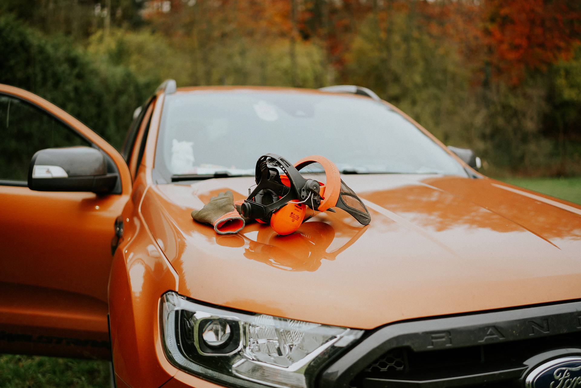 Schutzhelm und Arbeitshandschuhe liegen auf der Motorhaube eines orangefarbenen Ford Ranger von HG Rudolph.