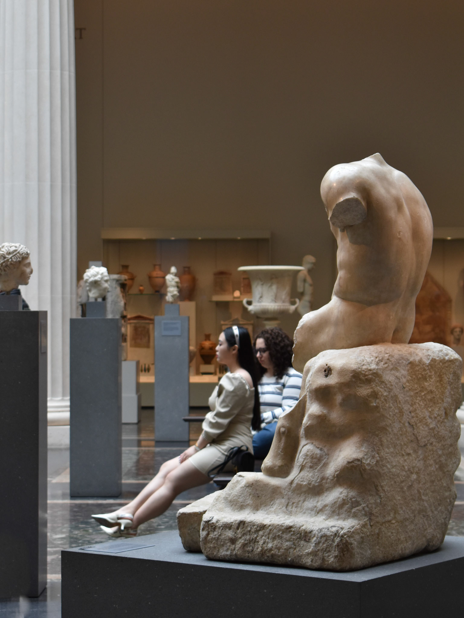 Statues: A woman sits in a statue section of Ancient Greece at the Met.
