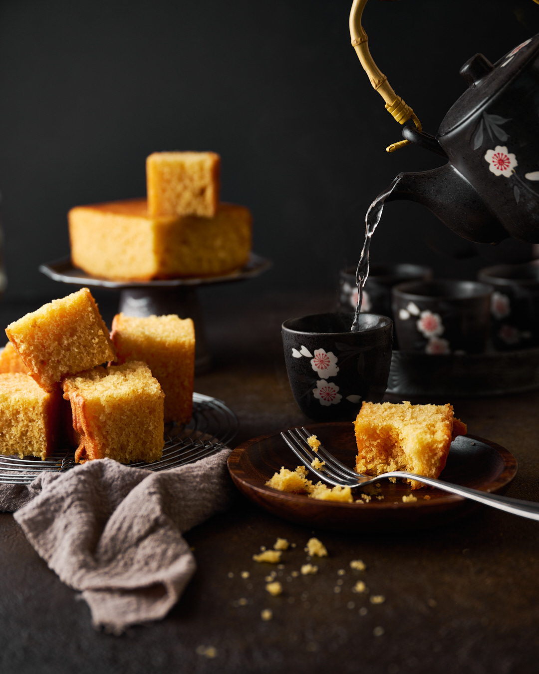 Beautiful butter cake on a plate with soe tea being poured in the background - dark and moody. Photographed by Anusha Stewart