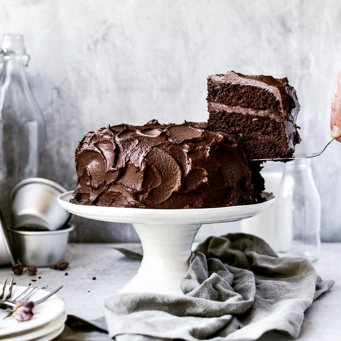 A gorgeous chocolate cake with textured chocolate buttercream frosting and a slice about to be served by Anusha Stewart