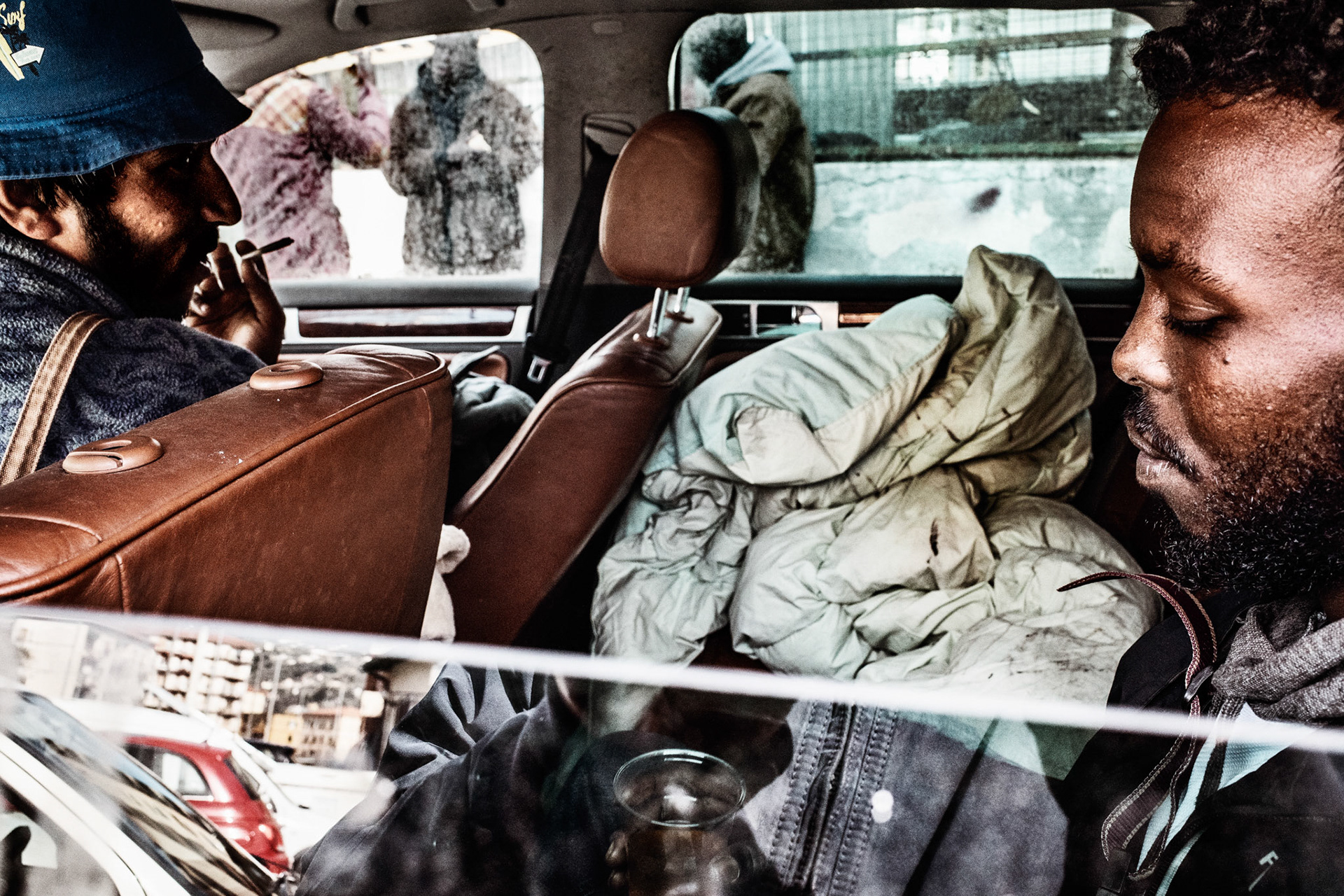 These two homeless men, Pakistani and Somali are smoking and drinking tea in a large abandoned car turned into a shelter where they spent many cold nights, an unhealthy shelter with an acrid smell