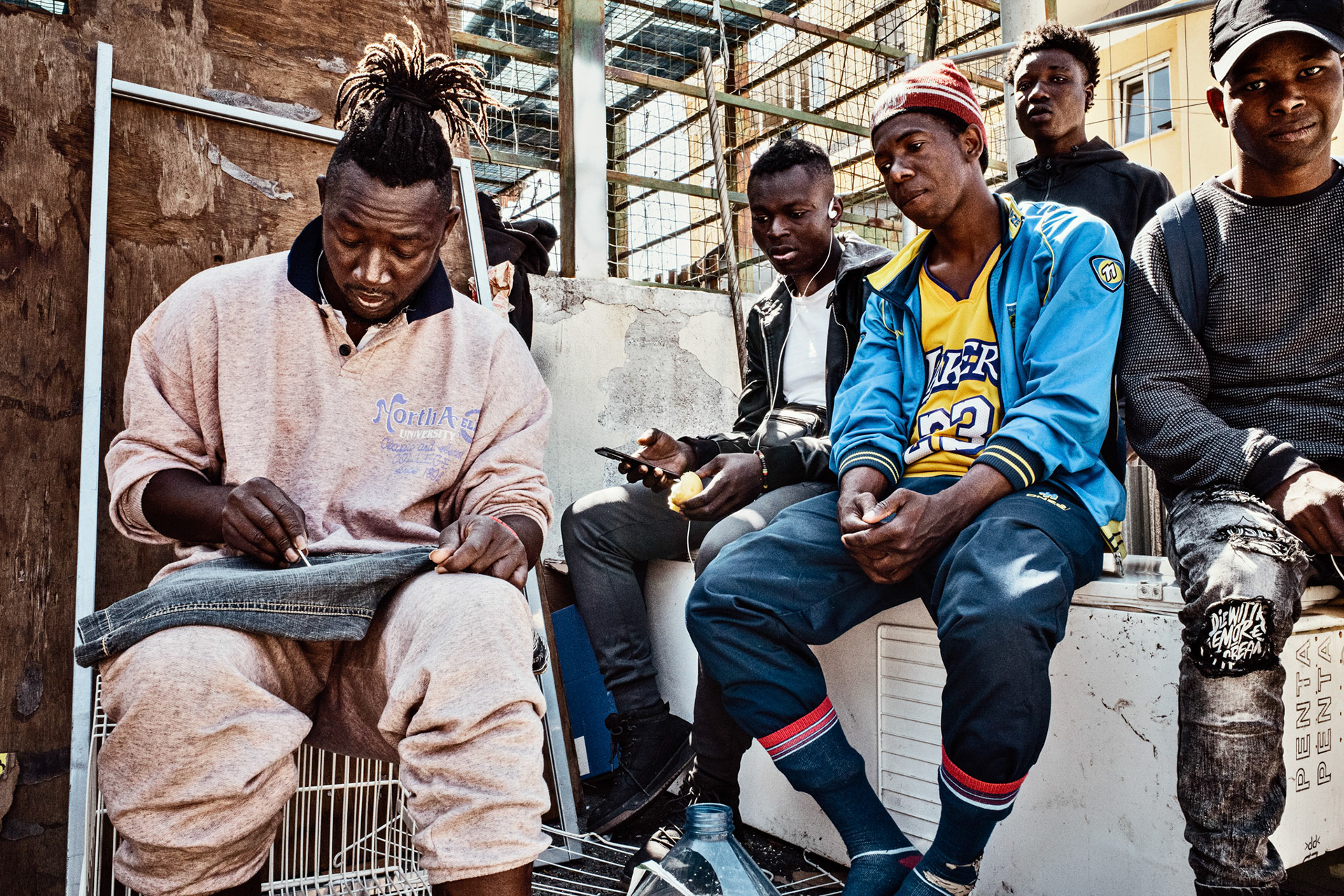 A. is writing his name on a pair of trousers, using a cotton bud soaked in bleach. The young boys at his side are sitting on a refrigerator found abandoned near the rubbish bins used as a wardrobe for blankets and clothes. These teenagers, originally from Guinea and the Ivory Coast, spent a very long time in Ventimiglia, waiting for the opportunity and the money to cross the border.