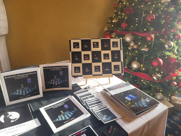 Photo graph of books postcards scenes and prints set up at a stall next to a Christmas tree.