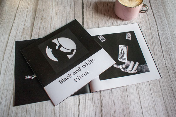 Photograph showing black-and-white Circus scene cover on top of open scene with photograph of a hand with a levitating card next to a cup of coffee.