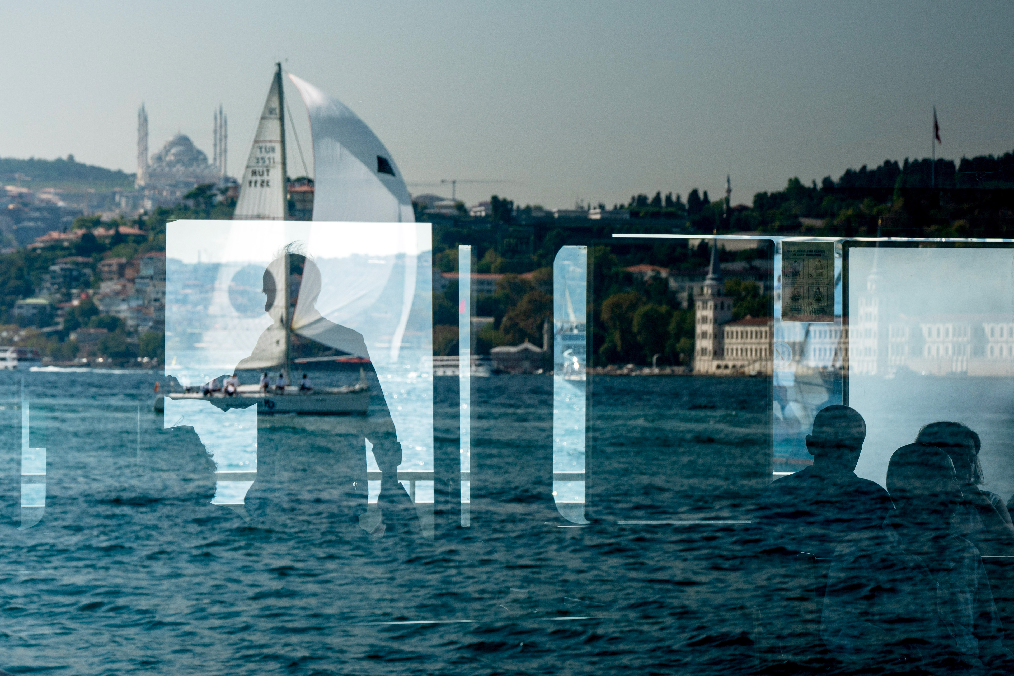 A view of a sailing team competing in the Bosphorus Cup sailing races, with the Buyuk Camlıca Mosque in the background, as people travel by ferry across the Bosphorus on September 23, 2023.