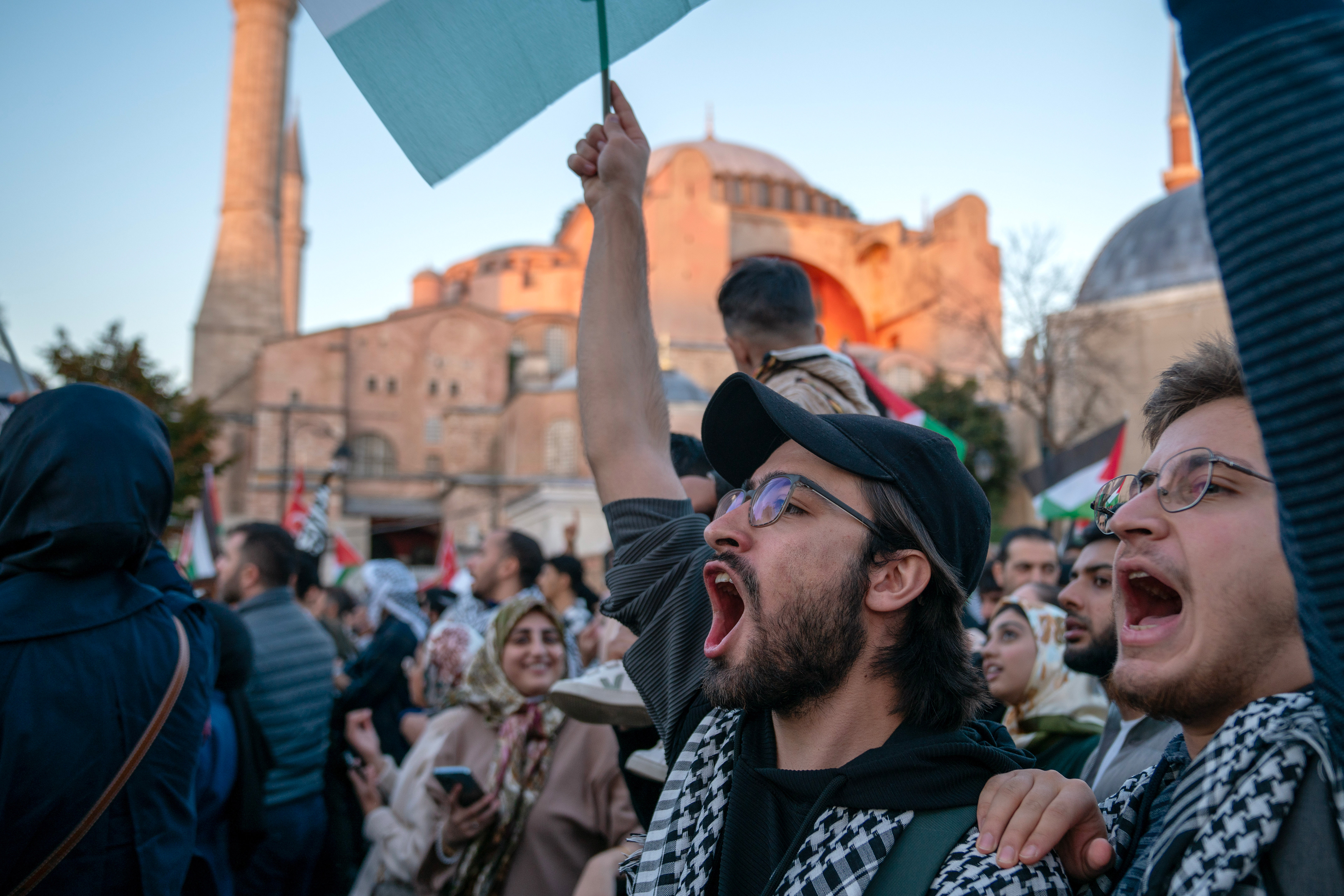 People are take part in a march support of Palestine shout slogans and wave flags at Sultanahmet Square in Istanbul, Turkey, with the Hagia Sophia Mosque in the background.
