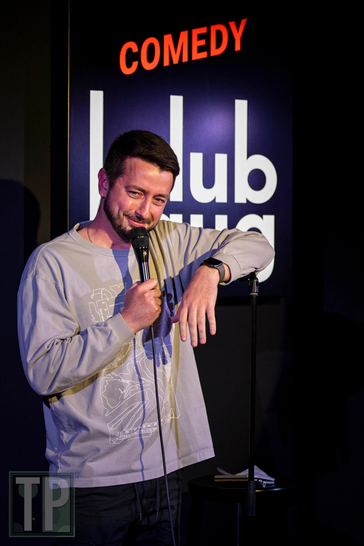 A live performance portrait of comedian Egor Fufachev on stage during an English open-mic set at Comedy Club Haug in Rotterdam, the Netherlands.