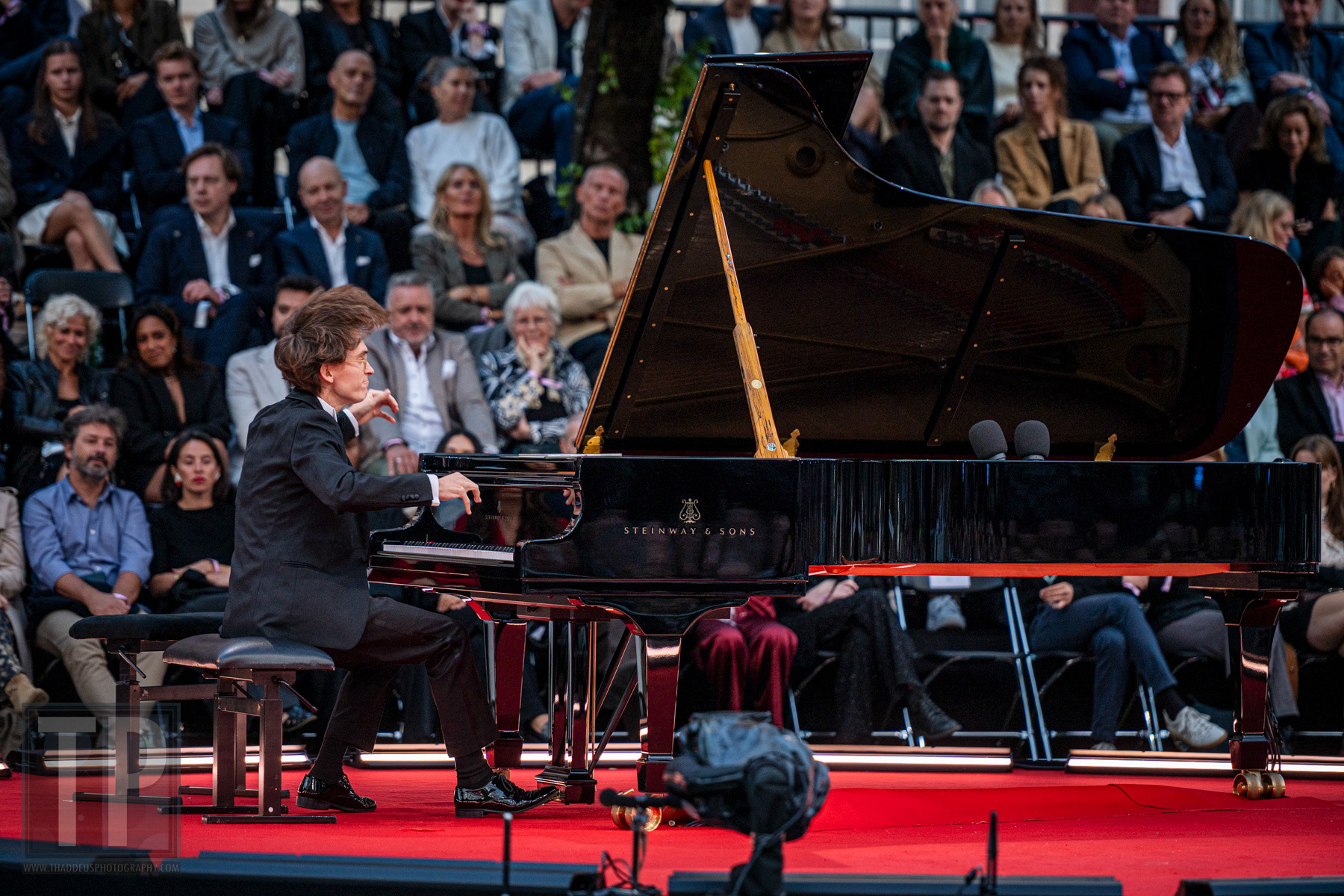 Pianist Shane van Neerden tijdens een solopassage aan de Steinway-vleugel, het publiek dichtbij langs het podium. Prinsengracht, Amsterdam, 22 augustus 2026. · Pianist Shane van Neerden during a solo passage at the Steinway grand, the audience close along the stage. Prinsengracht, Amsterdam, 22 August 2026.