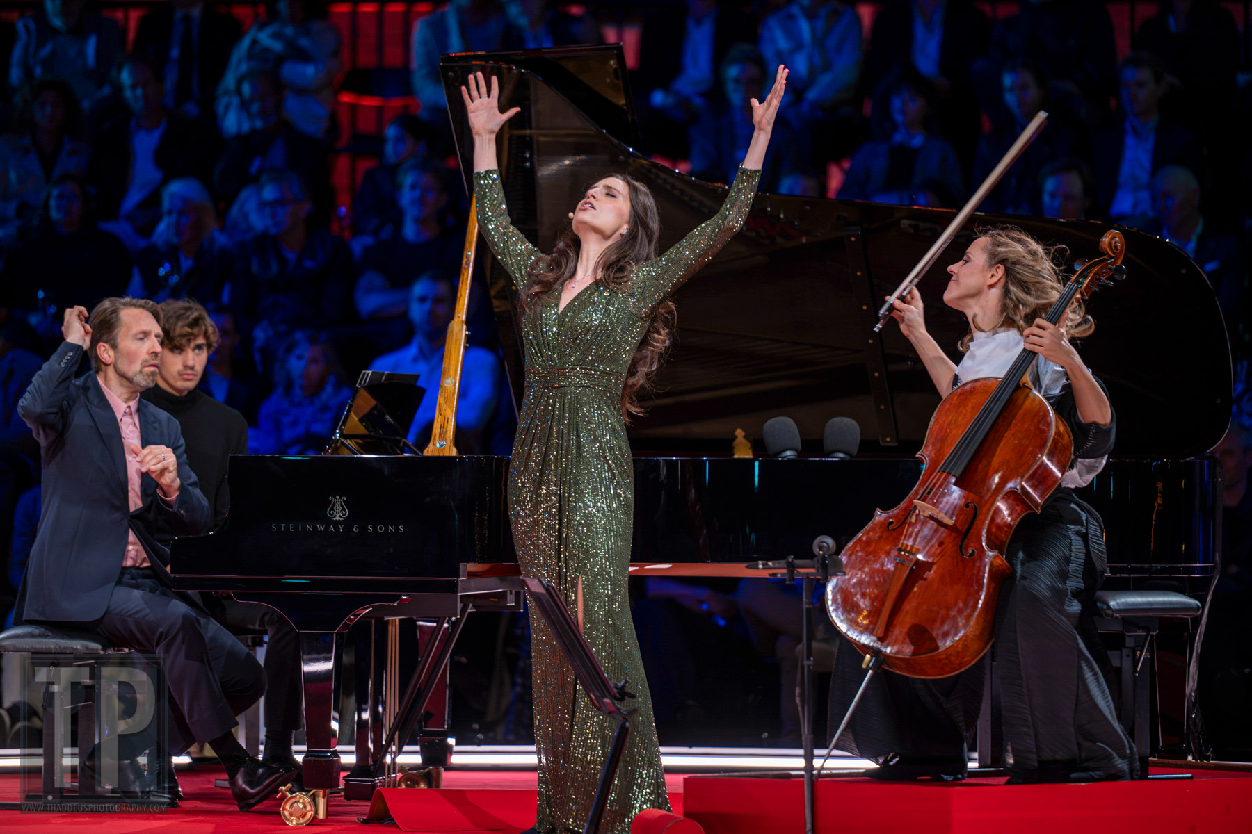 Mezzosopraan Maria Warenberg met opgeheven armen op het hoogtepunt van haar optreden, begeleid door pianist Leif Ove Andsnes en celliste Sol Gabetta. Prinsengracht, Amsterdam, 22 augustus 2026. · Mezzo-soprano Maria Warenberg, arms raised at the height of her performance, accompanied by pianist Leif Ove Andsnes and cellist Sol Gabetta. Prinsengracht, Amsterdam, 22 August 2026.
