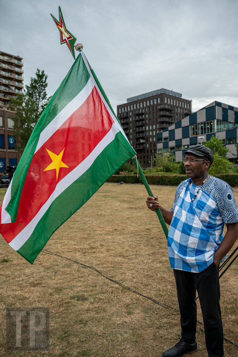 Een man houdt de Surinaamse vlag omhoog tijdens de Keti Koti-herdenking, Rotterdam. · A man holds the Surinamese flag aloft during the Keti Koti commemoration, Rotterdam.