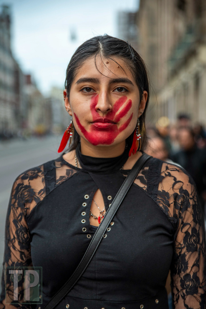 The Red Hand Print in Native American tradition symbolizes solidarity with missing and murdered indigenous women and girls. It can also symbolize the silencing and oppression of Native American groups. The person in this portrait explained they wore the Red Hand Print in solidarity with the Two-Spirits belief of a third gender that embodies masculine and feminine spirits.