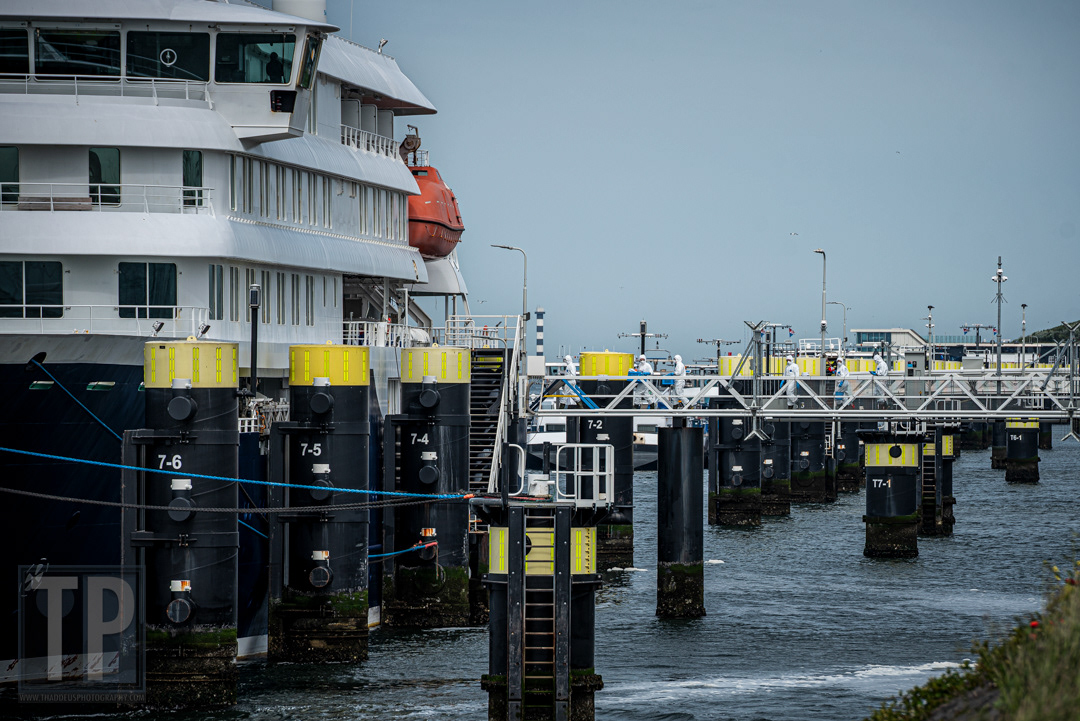 Leden van het ontsmettingsteam in volledige beschermende kleding lopen over de loopplank aan boord van de MV Hondius, aangemeerd aan de kade in de haven van Rotterdam na de uitbraak van het Andes-virus, 19 mei 2026. · Members of the disinfection crew in full protective clothing walk up the gangway to board the MV Hondius, moored at the quay in the port of Rotterdam following the Andes virus outbreak, 19 May 2026.