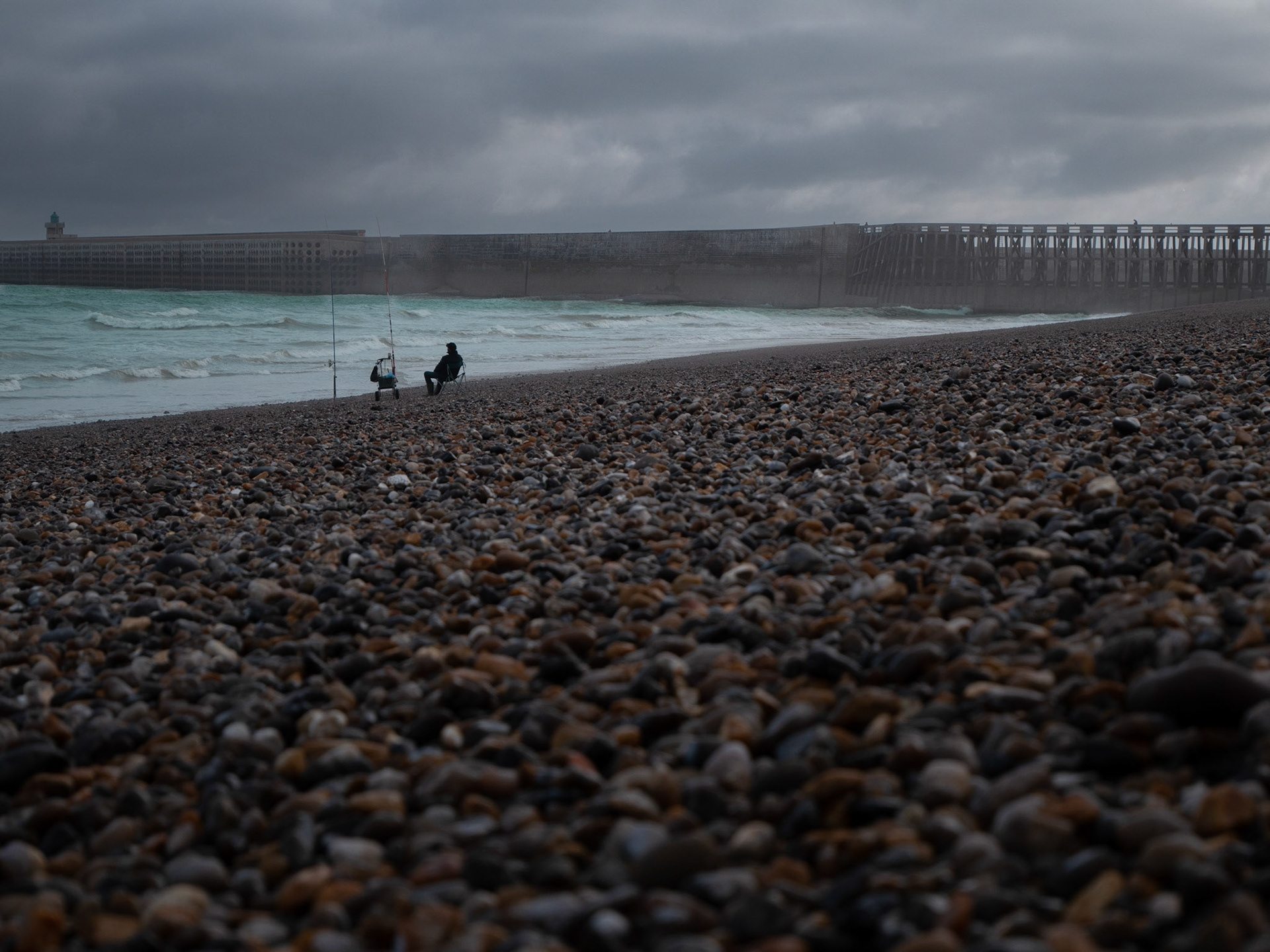 Pecheur sur la plage de Dieppe. Vue sur la jetée du port.