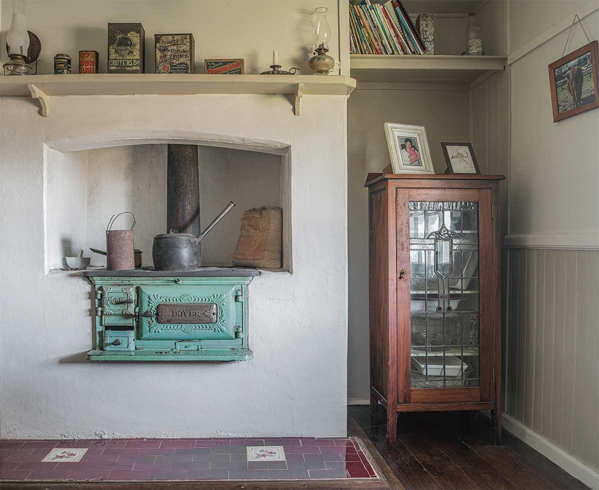 The original one room house that now serves as our dining room. The fuel stove C1936 would have been added into the original fireplace then sealed and render placed around it as the room is C1880. Lines are visible where the filling took place. Originally a metal pot crane would swing pots over an open fire for cooking. A pianola roll cupboard, restored by us in 1995 is proudly placed by it