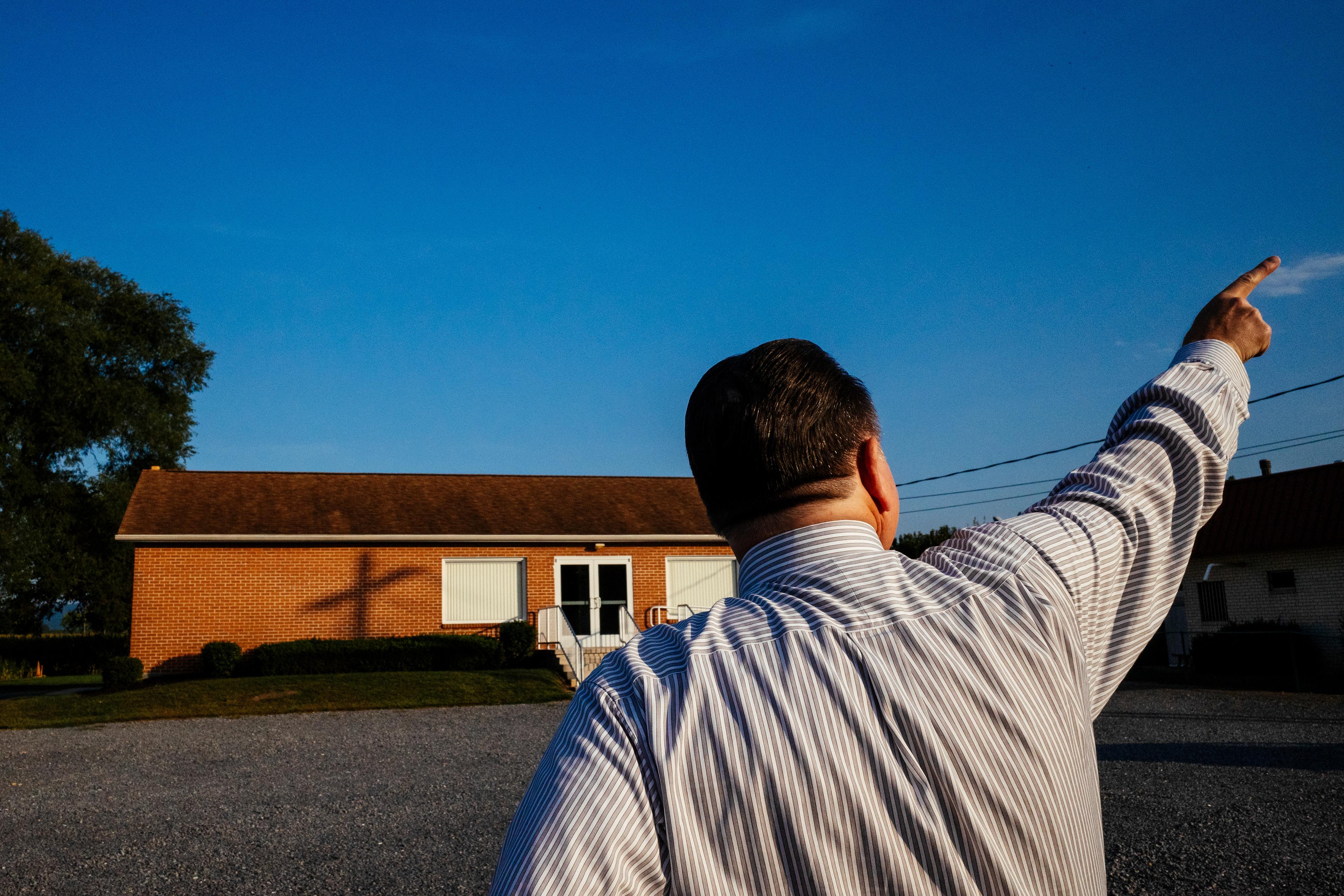 A pastor of a small church pointing to the source of the crucifix shadow, near Greencastle, PA, 2024