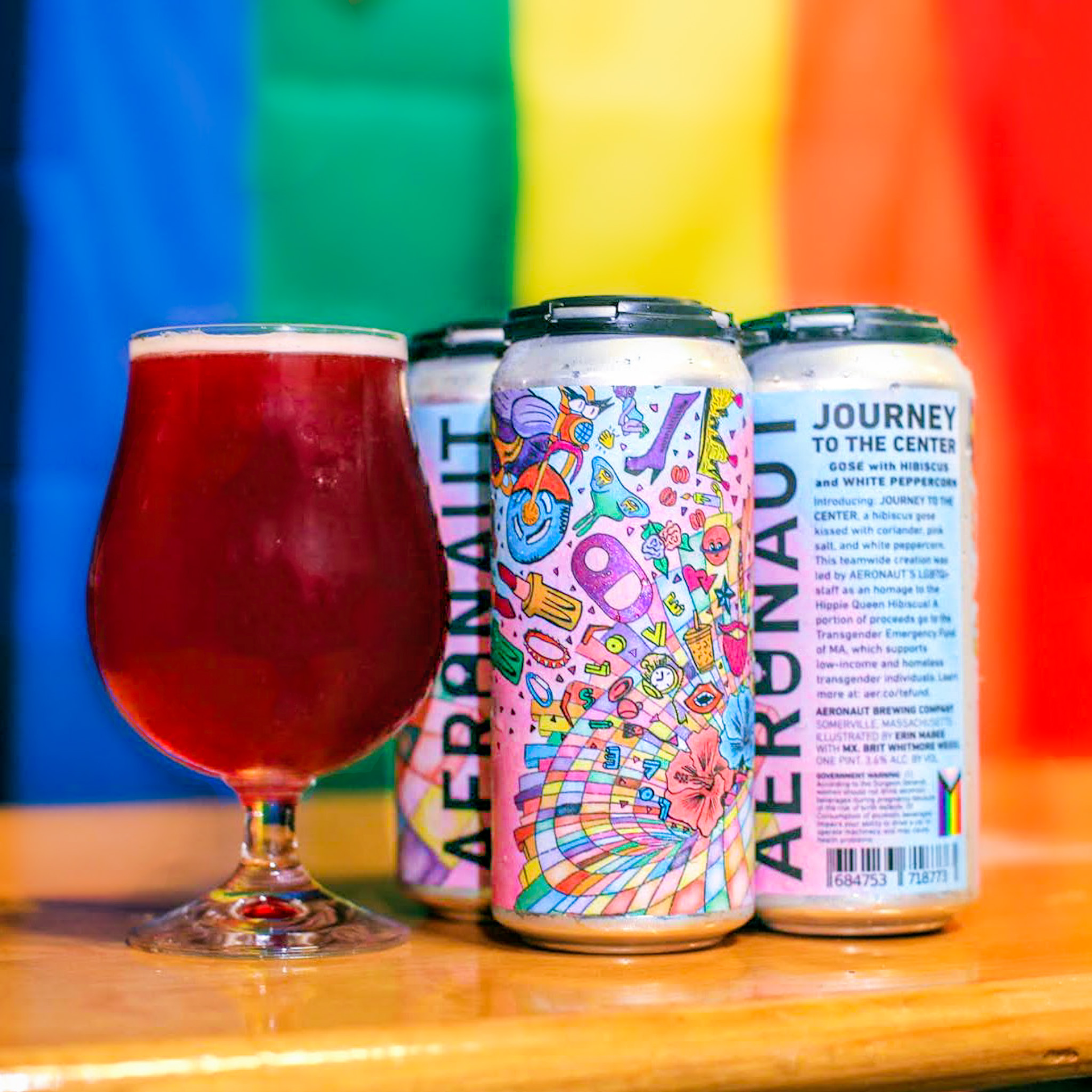 A picture of the beer in a can with a glass of the beer that is a bright red in front of a pride flag