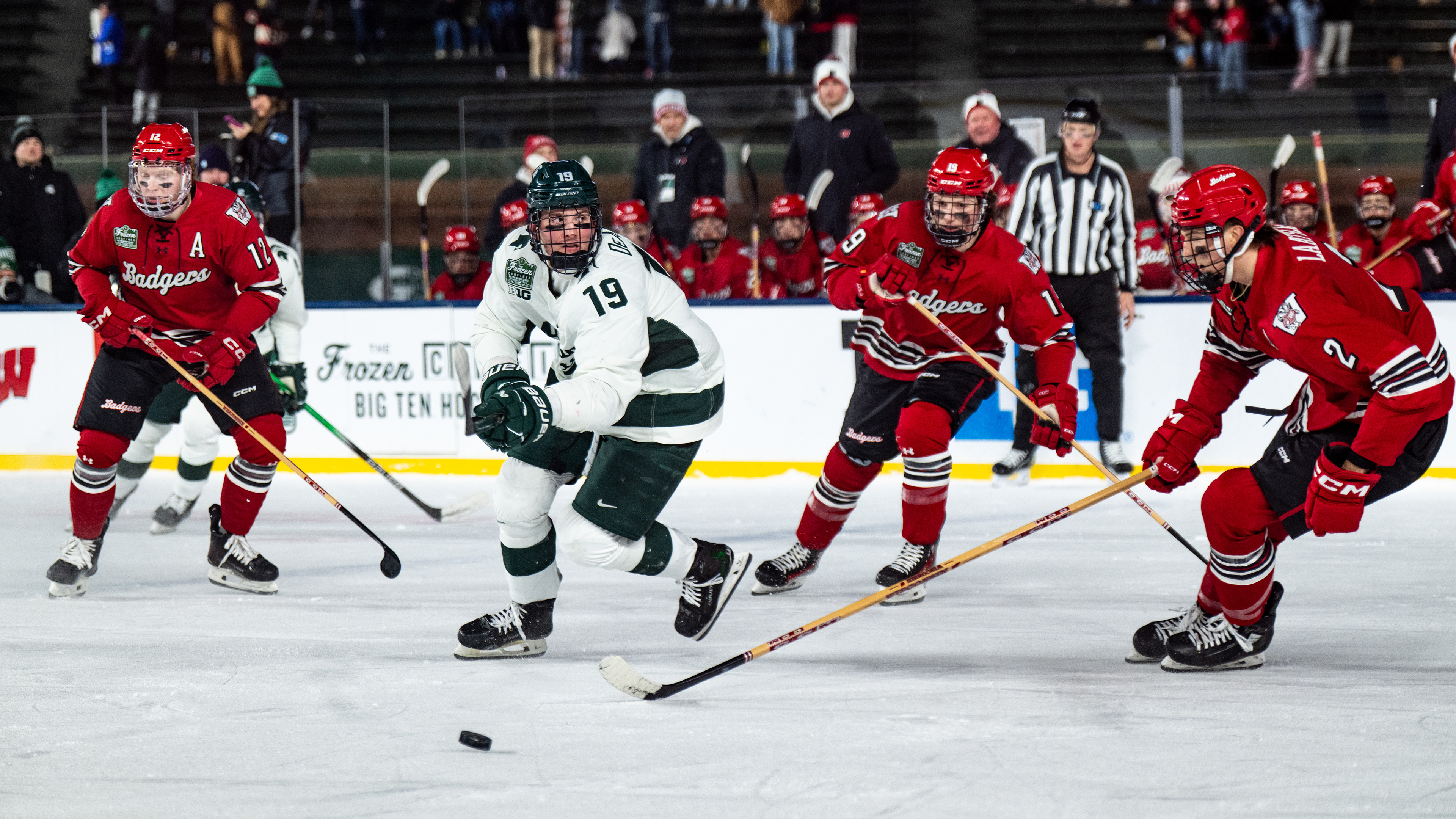 Michigan State freshman forward Mikey DeAngelo (19) tracks down the puck at Wrigley Field in Chicago on Jan. 4, 2025. The Spartans' junior forward Daniel Russell (20) netted the overtime winner with under two seconds remaining, earning the weekend sweep over the Badgers.