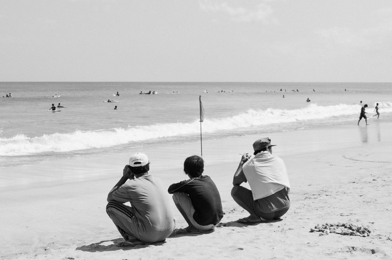 Beach boys casually squatting by the shore. Kuta, 2014.