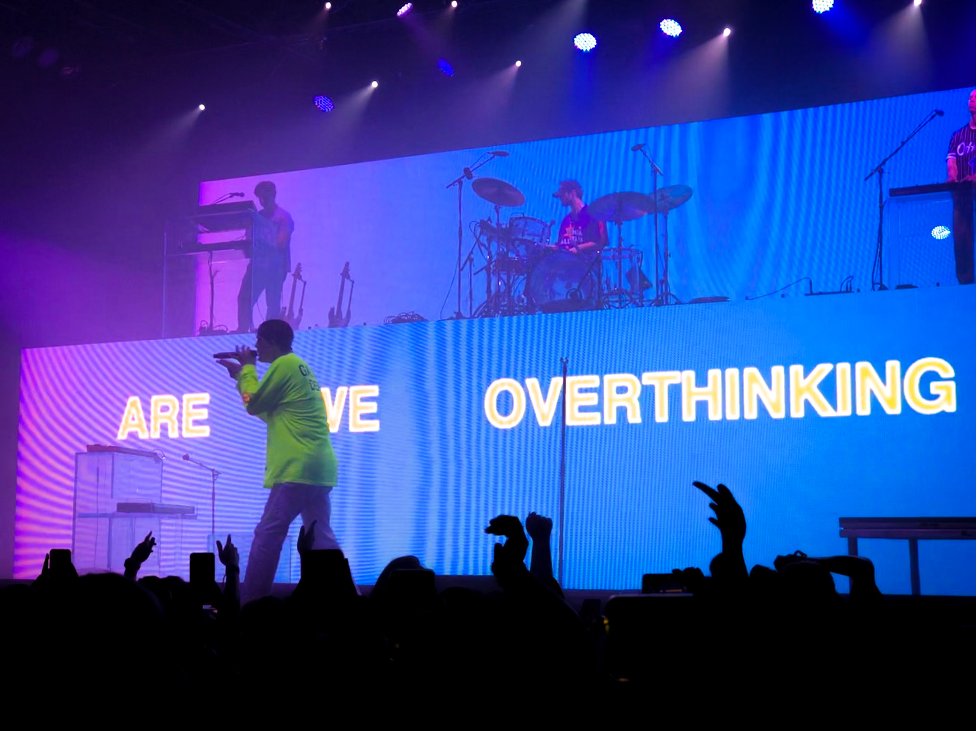 Image of Lany with OVERTHINKING digital text in the background, image taken from the crowd on an iphone x