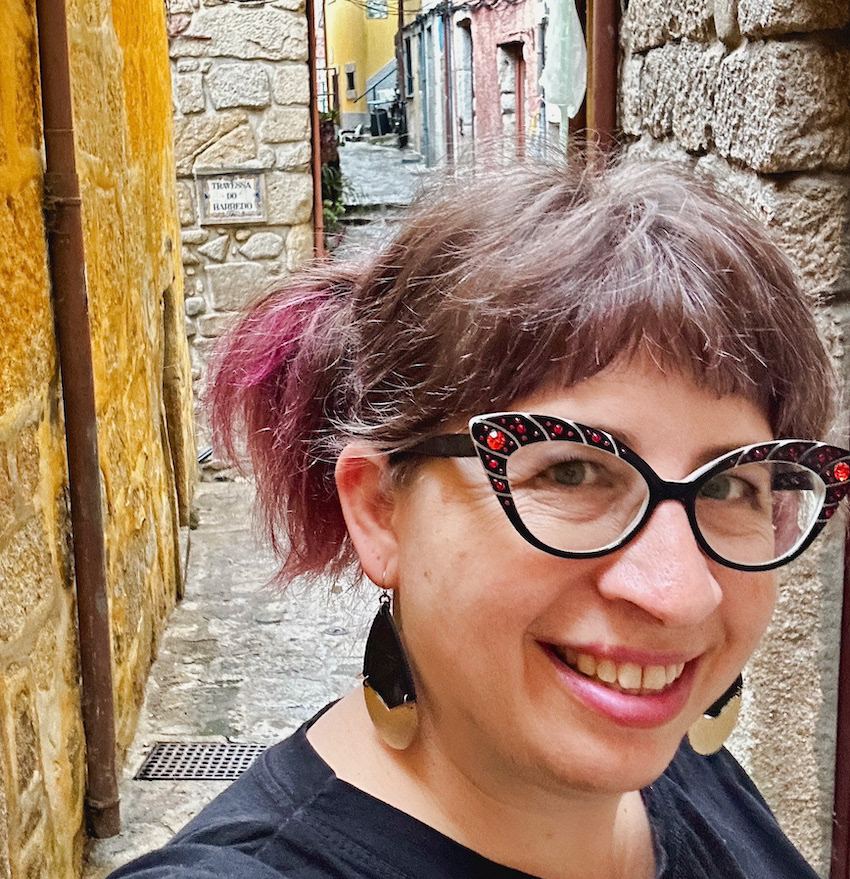 Jenn Alvin, woman with glasses and a ponytail taking a selfie in a cobblestone alley