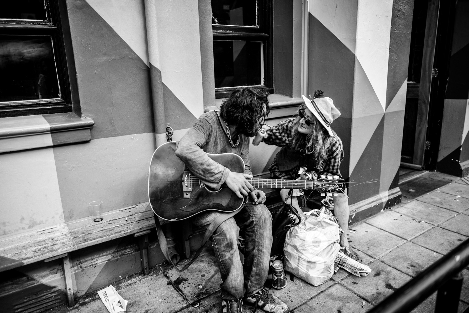 Man spraying a can into a guitarists mouth on a bench outside a pub. Image © Nik van Herpt
