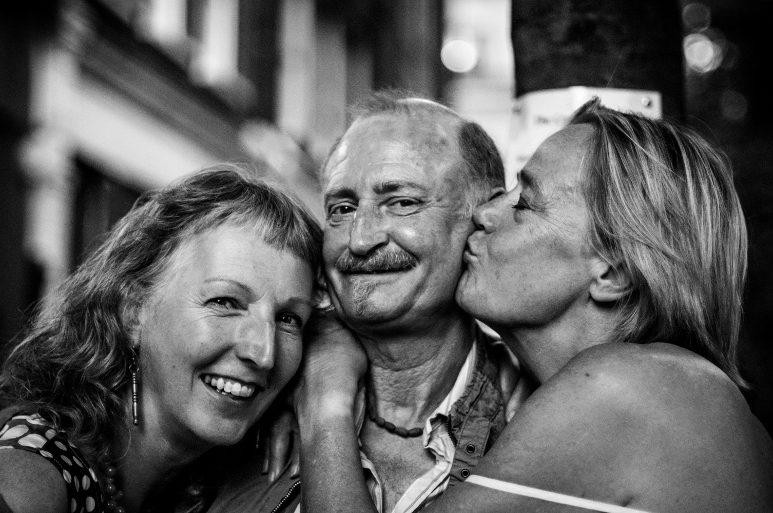Man between two women, outside a Soho pub, receiving kisses. Image © Nik van Herpt