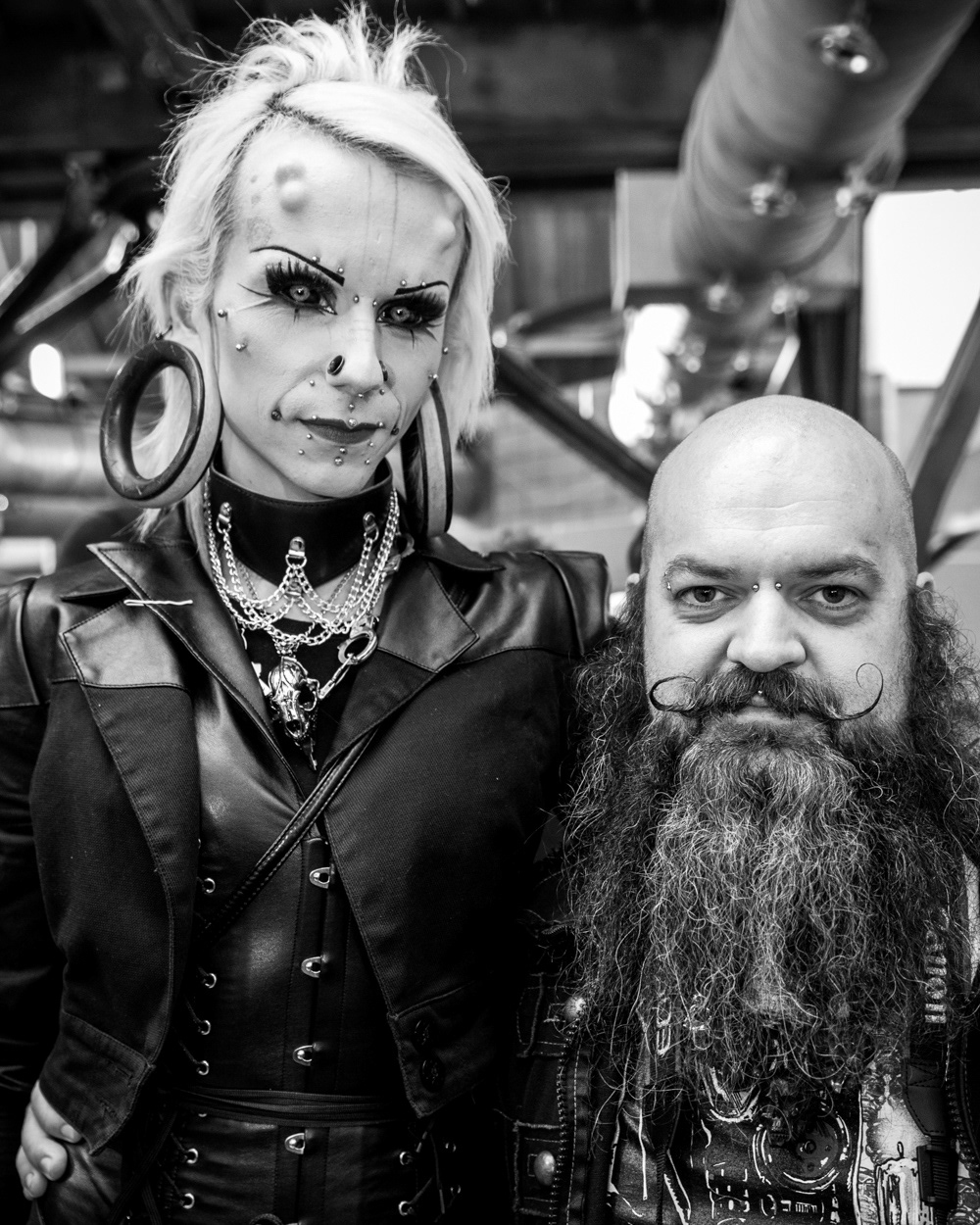 Tall person with face modifications standing next to shorter, bearded man. Image © Nik van Herpt