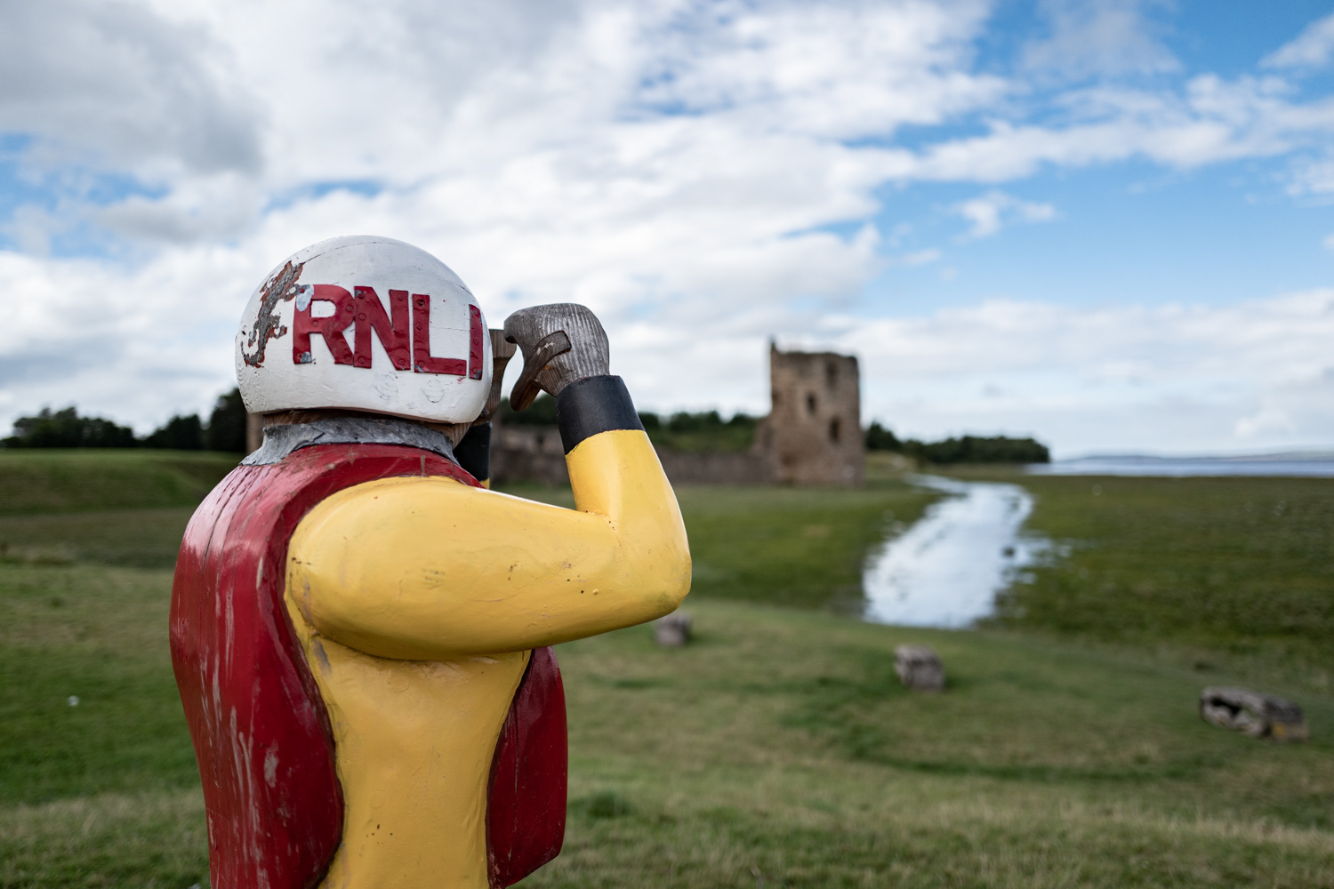 Wooden statue of an RNLI volunteer scanning the Dee Estuary, with Flint Castle in the distance, Wales. Image © Nik van Herpt