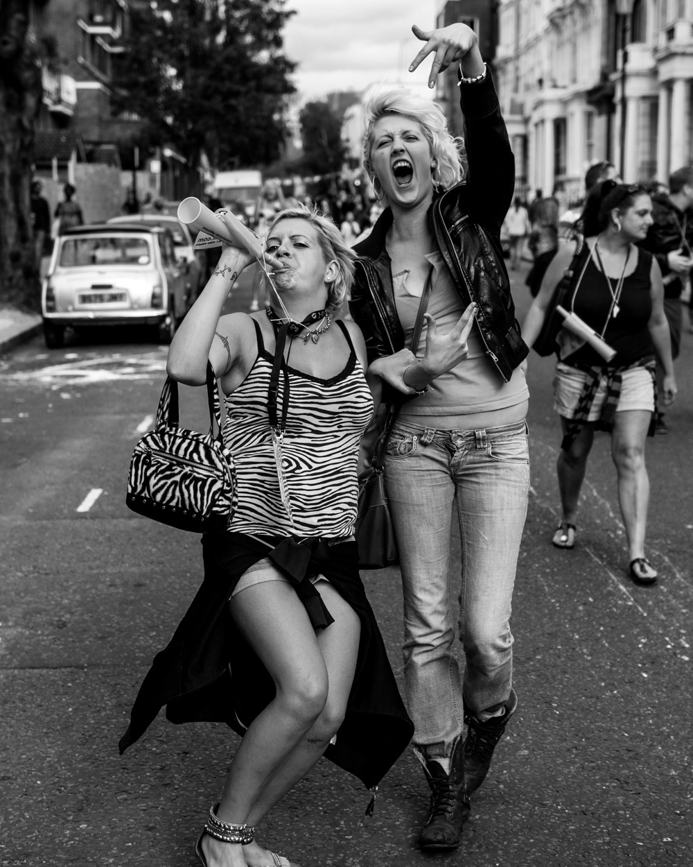 Two women partying down the street, blowing a trumpet and yelling. Image © Nik van Herpt