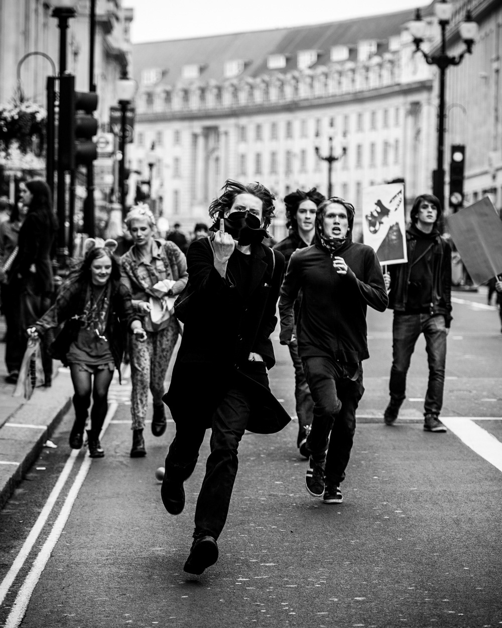 Masked youth running up Regent Street giving the middle finger at the 2011 anti-cuts protest in London. Image © Nik van Herpt