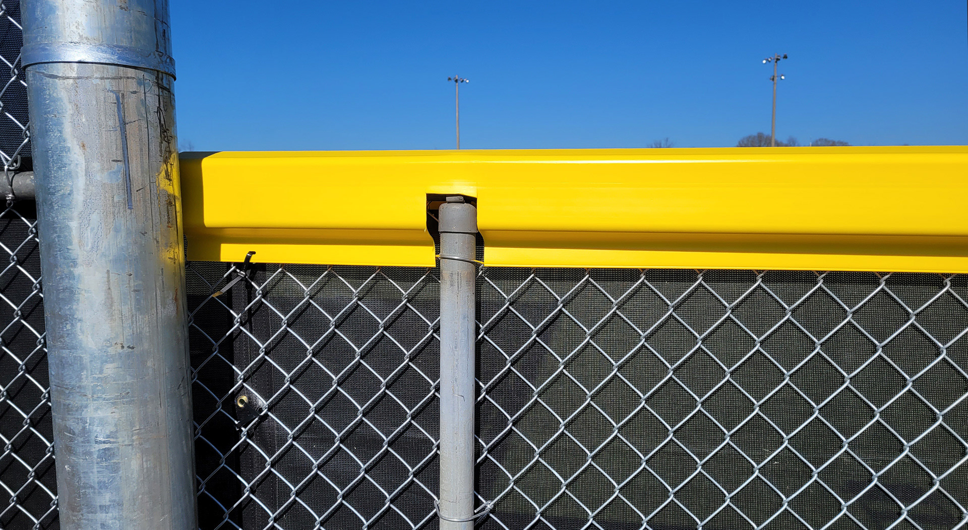 closeup of the backside of black fence windscreen and yellow D-style safety top cap affixed to a fence