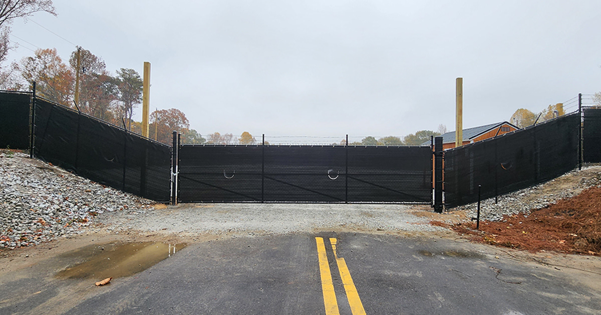 Close-up of a fence surrounding a business, covered with black privacy windscreen, showing moon vents and the installation detail on the fence entry door to the premises.