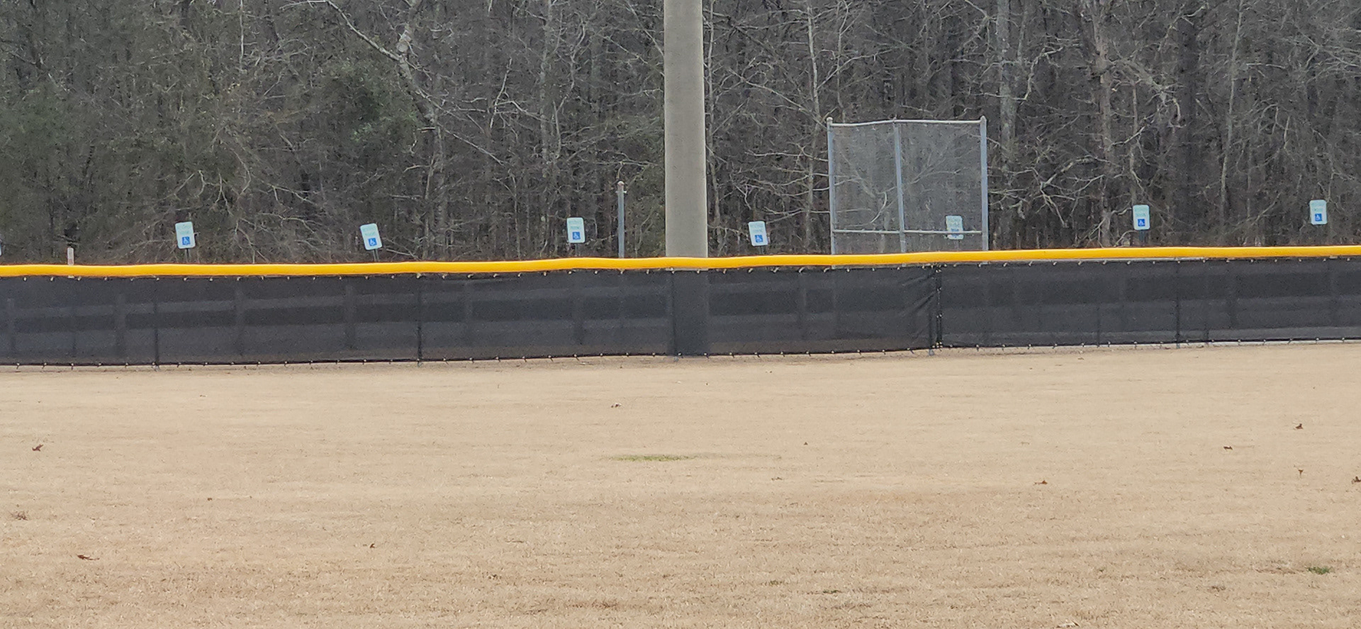 black fence windscreen with half moon vents, black zip ties and brass grommets surrounding a baseball field, fence topped with yellow poly-cap corrugated rail top fence cap