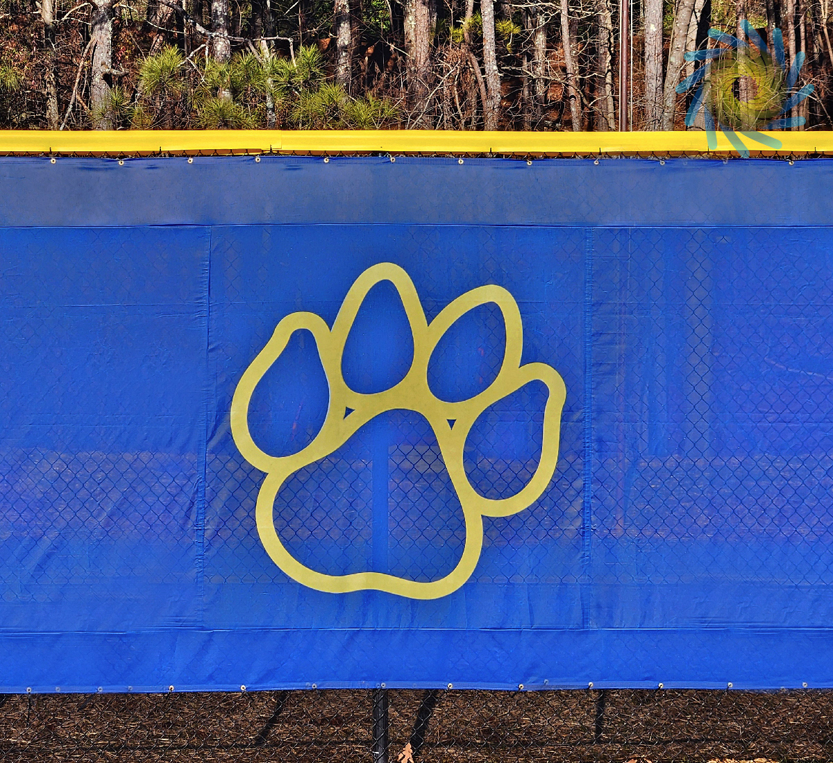 blue windscreen attached printed with a yellow paw print outline attached to a fence barrier on the outer edge of a baseball field