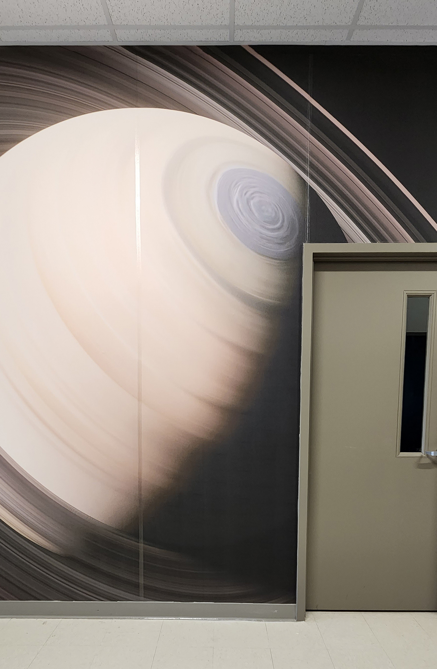 A floor-to-ceiling adhesive vinyl wall mural in a hallway, surrounding a closed door. The mural features an image of Saturn with dark space in the background. 