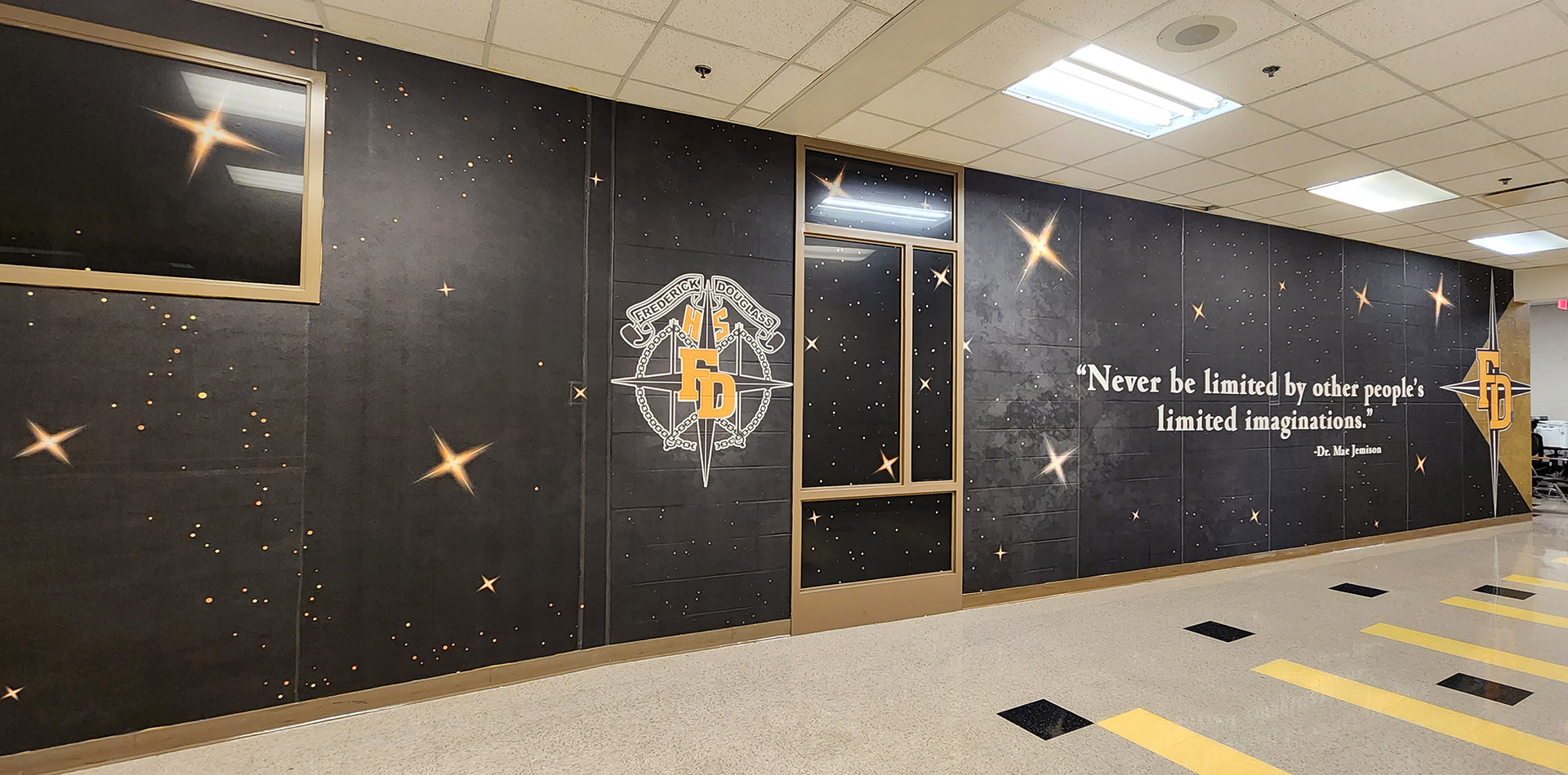 full print adhesive vinyl wall mural and window perf printed with gradient white and yellow stars on an all black background underneth a logo reading 'fredrick douglass HS FD' and a quote reading "Never be limited by other people's limited imaginations. - Dr. Mae Jemison" and a 'FD four point star logo'