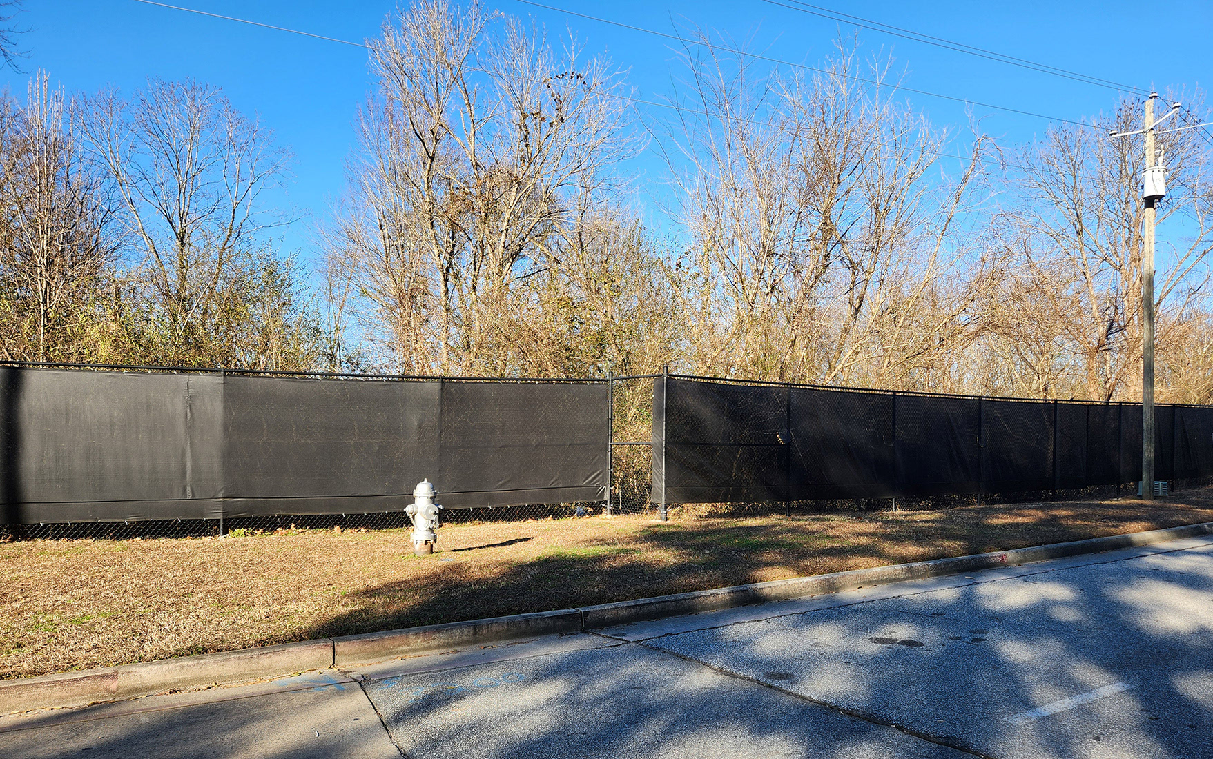 , "black fence windscreen on a fence along the side of a road"