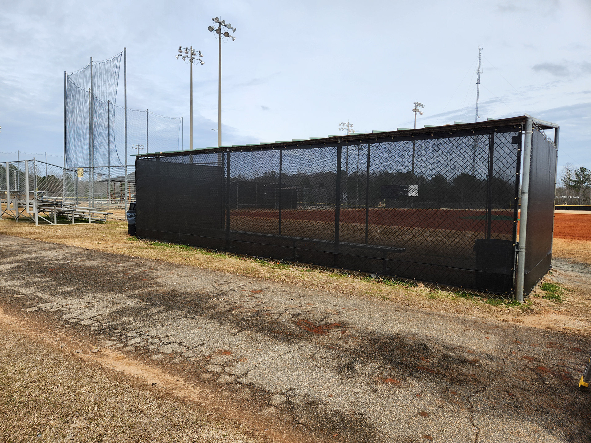 black fence windscreen with half moon vents, black zip ties and brass grommets surrounding a baseball field dugout