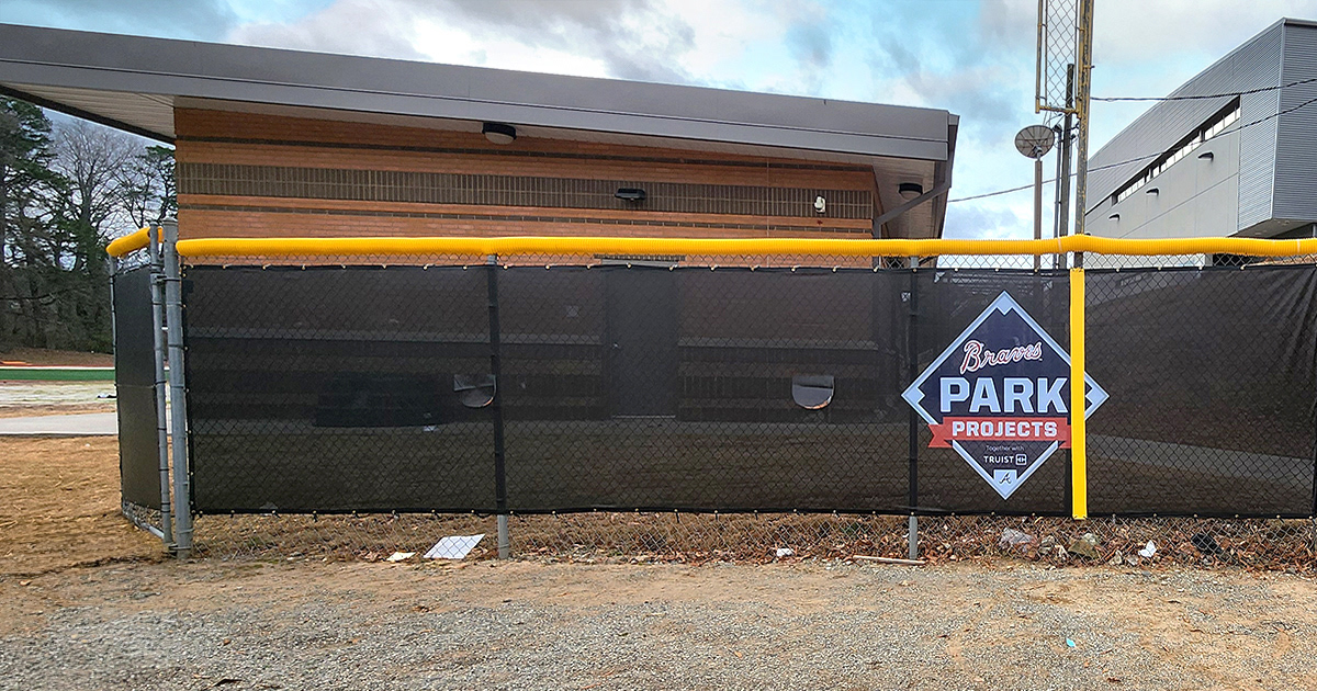 black fence windscreen printed with a navy, red and white logo reading 'braves parks projects', topped with a yellow fence guard rail top tear drop fence cap