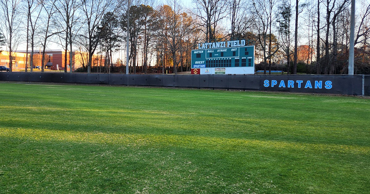 black fence windscreen printed with blue lettering outlined in a lighter shade of blue reading 'Spartans' in a baseball outfield