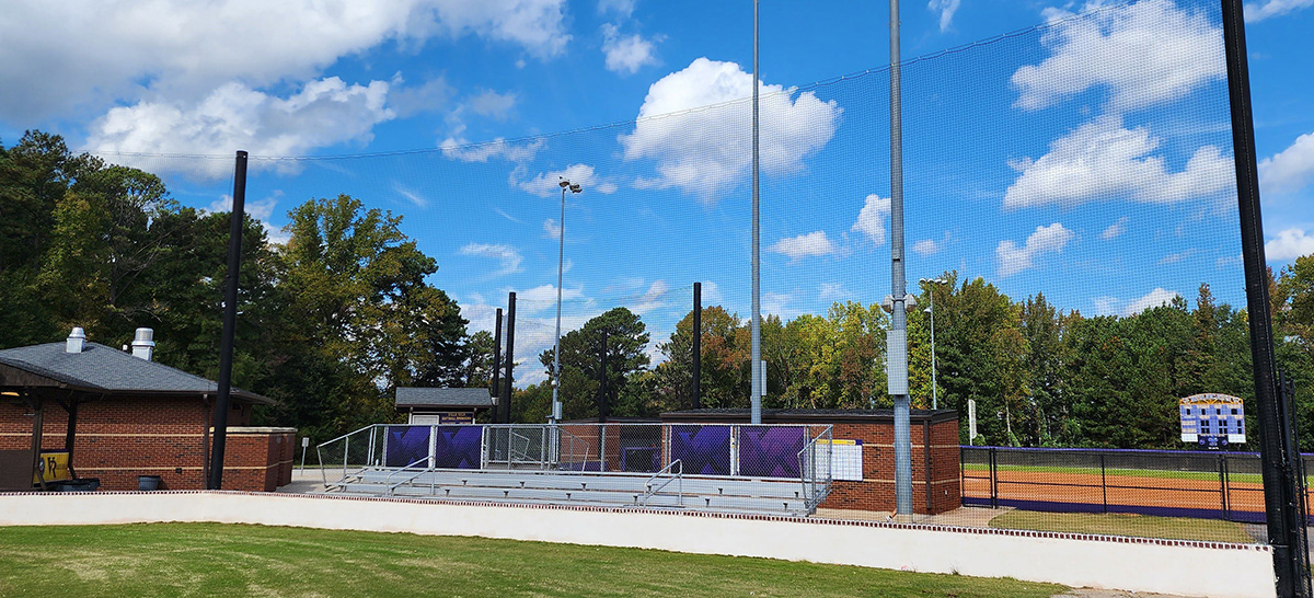 Black sideline sports netting surrounding a baseball field, positioned behind a set of bleachers.