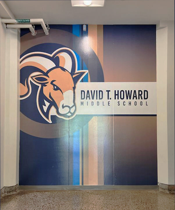 A floor-to-ceiling adhesive vinyl wall mural featuring the image of a ram in the top left, a white bar in the middle with the text 'DAVID T. HOWARD MIDDLE SCHOOL' in navy blue, and a gradient blue and orange background with blue and orange stripes vertically down the middle. 