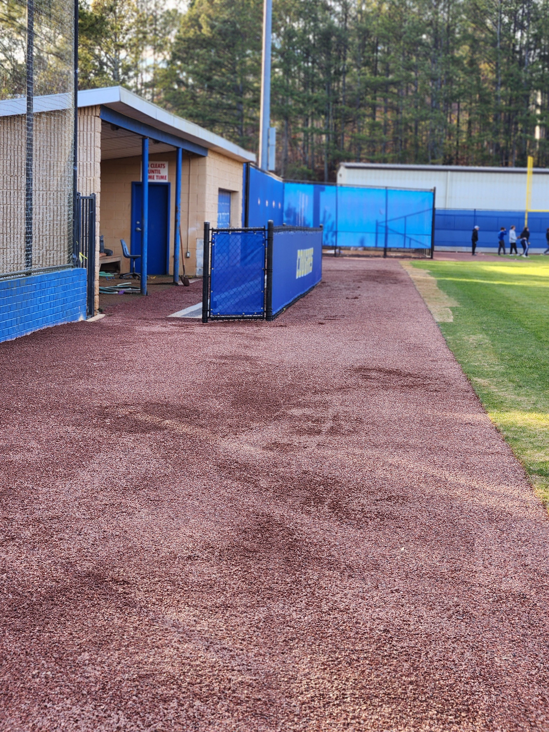 blue windscreen printed with yellow text outlined in white reading 'cougars' attached to a fence barrier surrounding a baseball dugout, blue windscreen attached to fencing along the baseball field edge