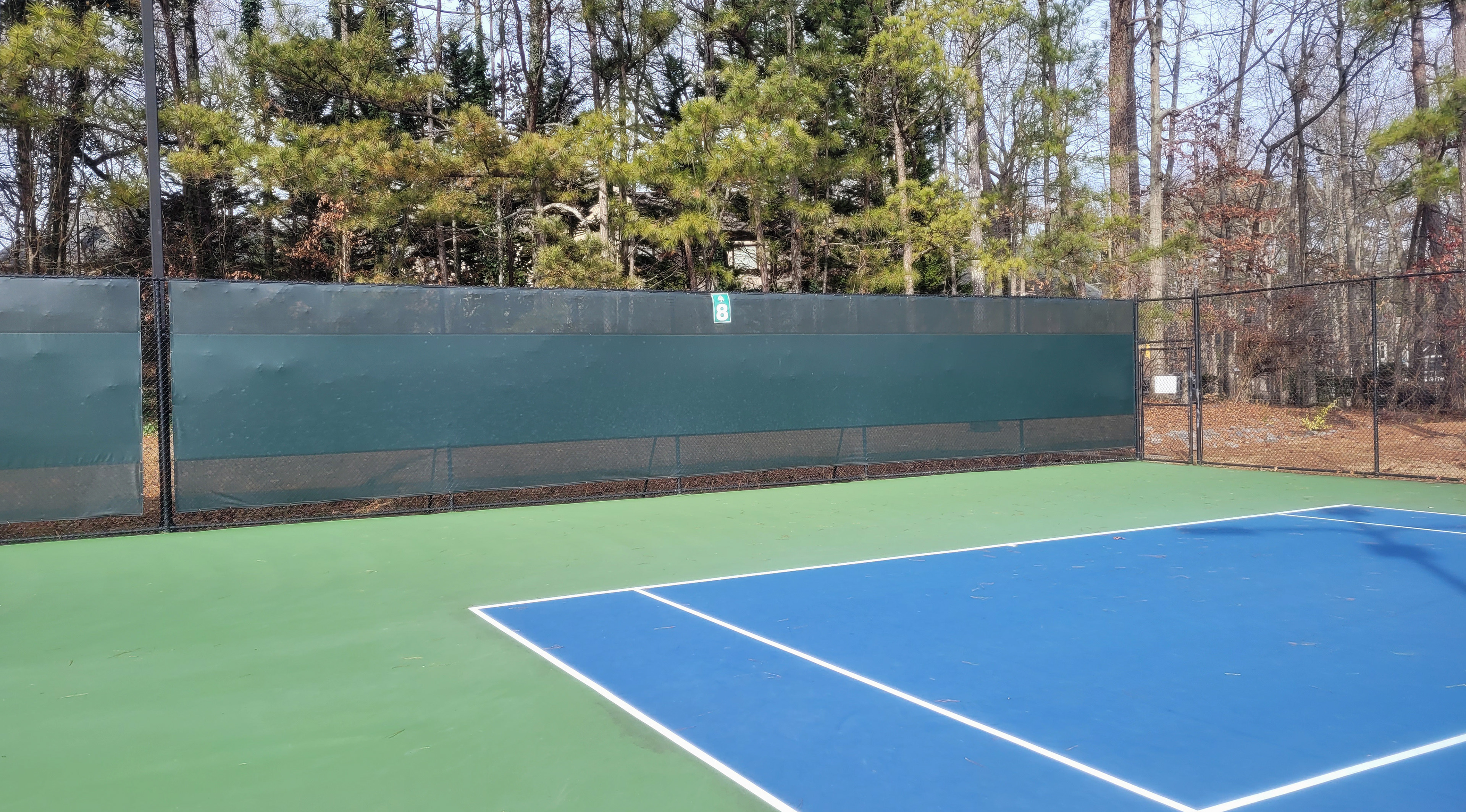 green fence windscreen bordering a tennis court